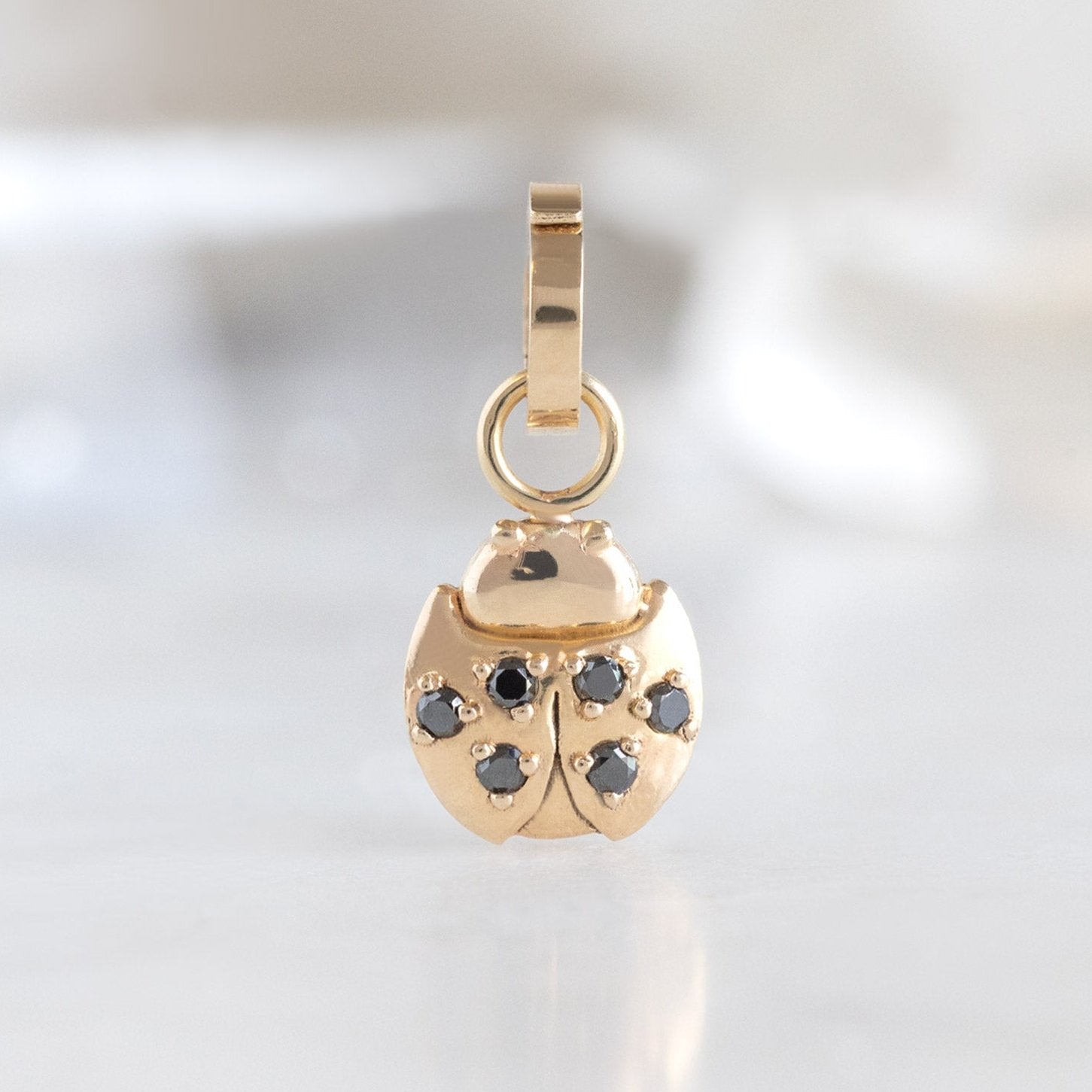 The Ladybug Charm in 10K Yellow Gold on White Marble