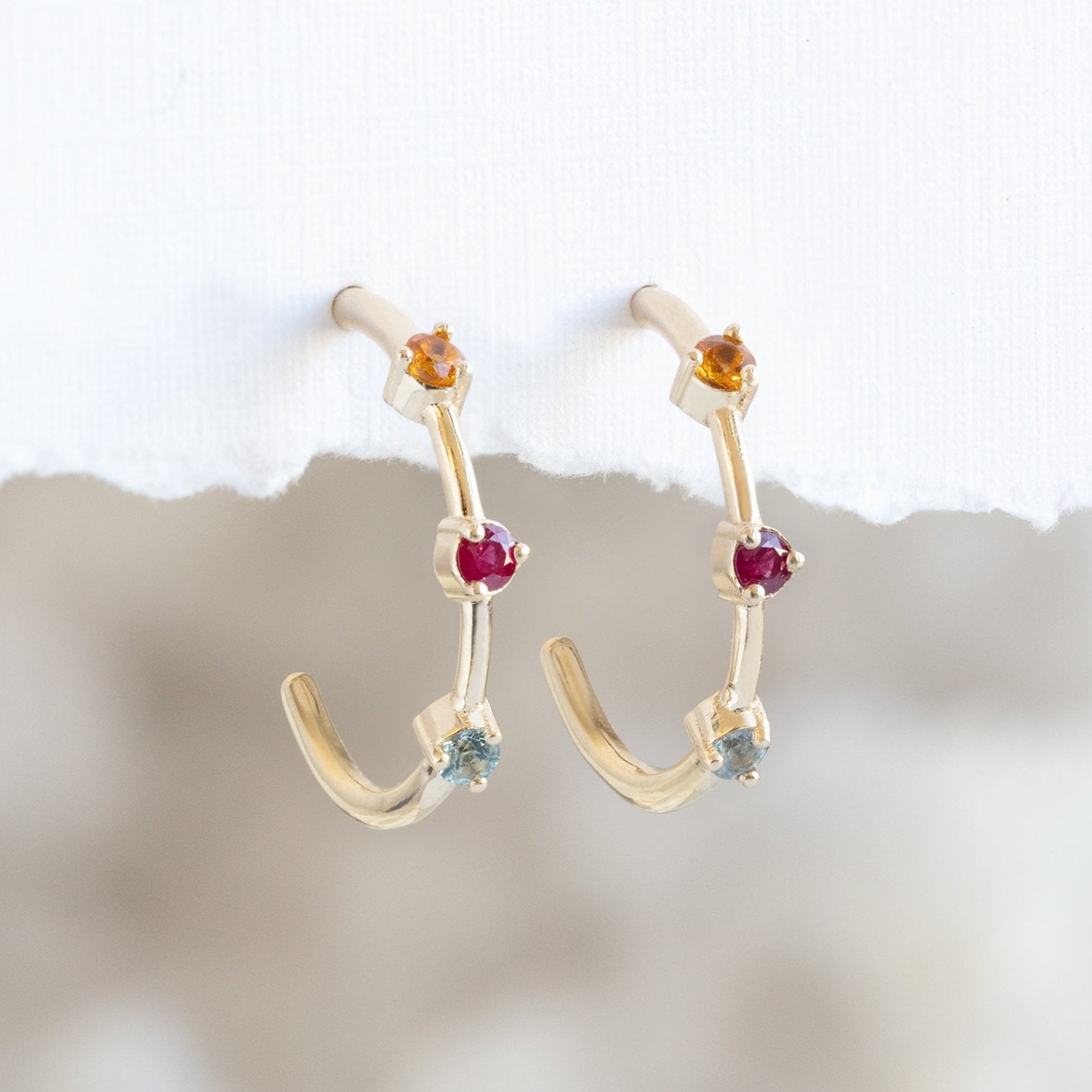 The Custom Multi-Birthstone Hoops 3 Stone Option Hanging on White Textured Paper