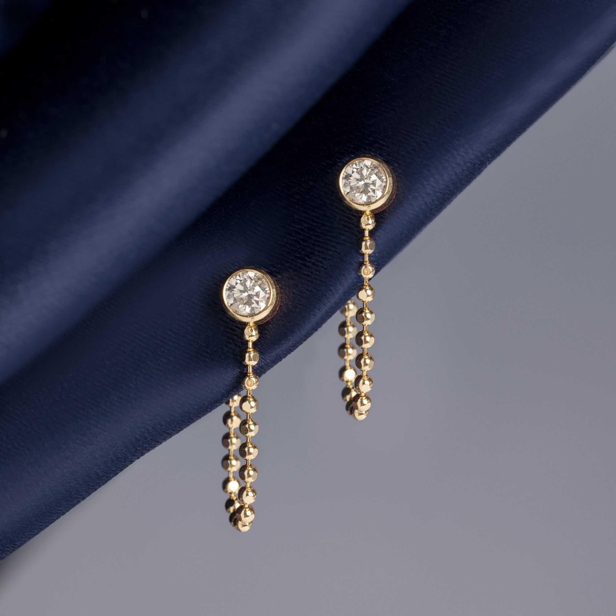 Diamond Chain Hoop Earrings in 10K Yellow Gold hanging on navy blue fabric