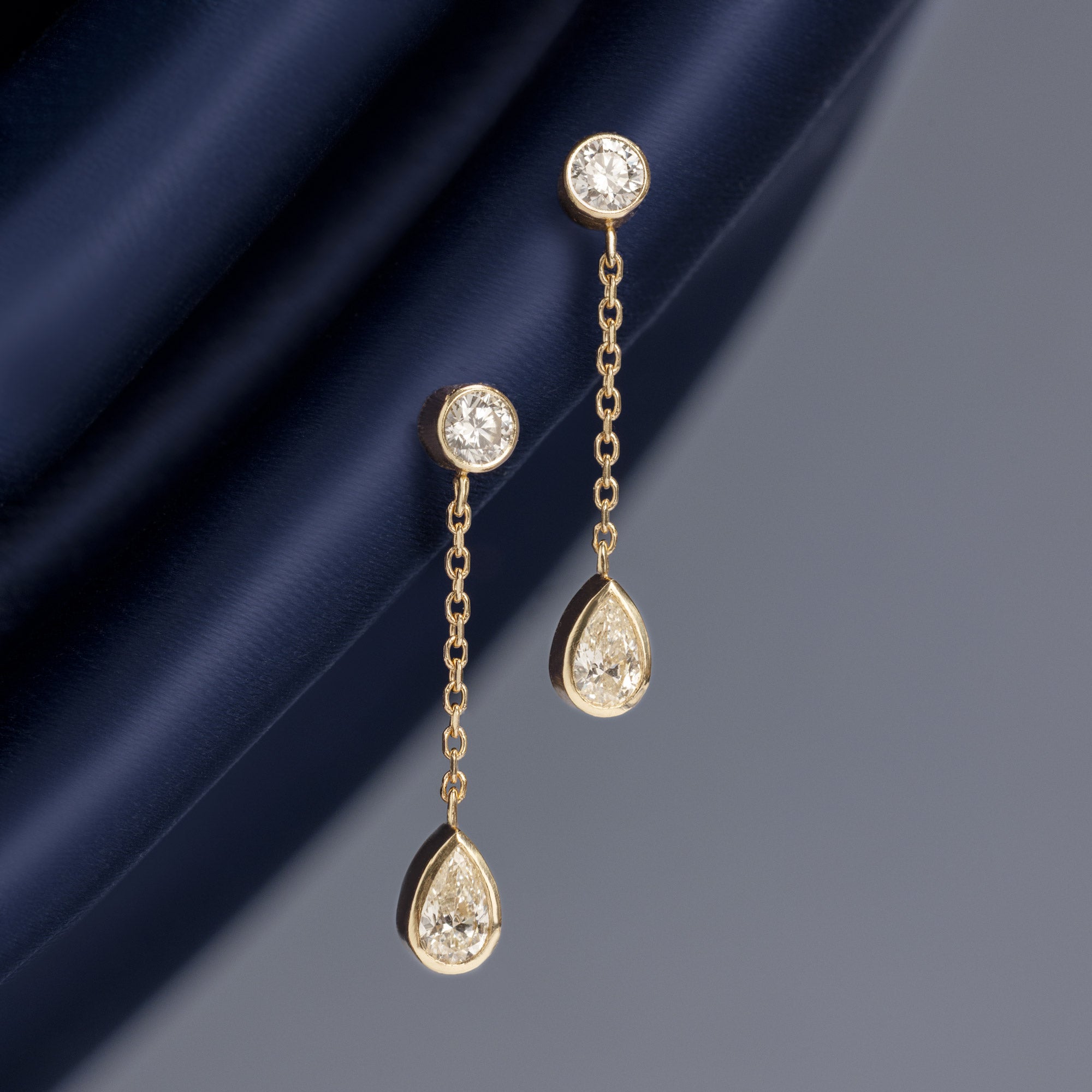 ‘Date Night’ Pear Diamond Drop Earrings in 10K Yellow Gold hanging on navy blue fabric