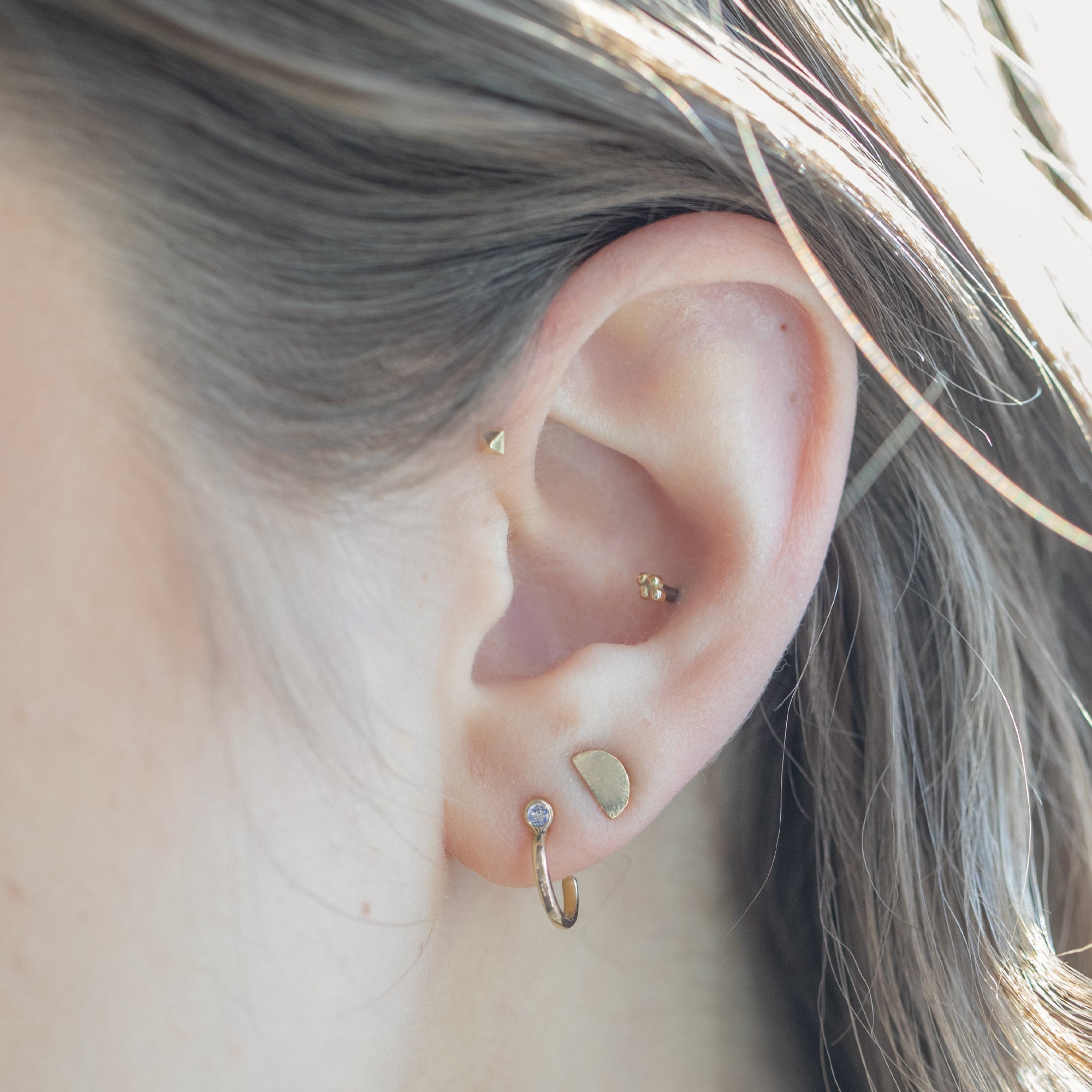 Custom Moonstone Birthstone Hoop Earrings | 14K Yellow Gold. Displayed on model's ear with additional stud earrings. 