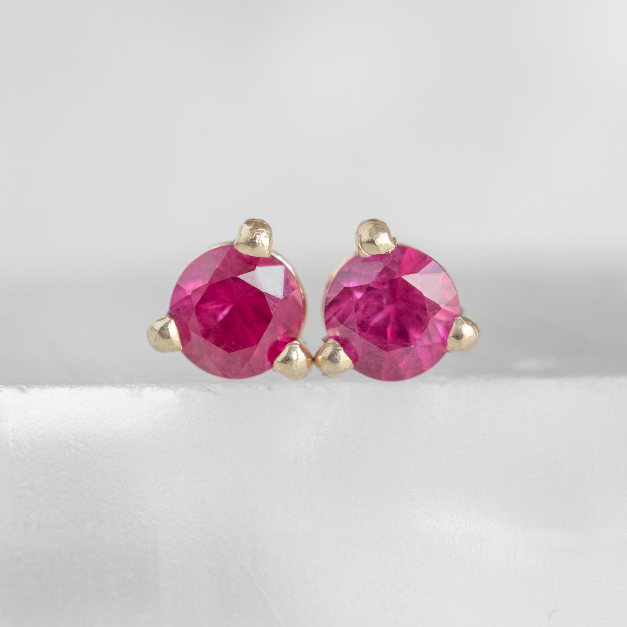 The Ruby Stud Earrings in 14K Yellow Gold on White Marble