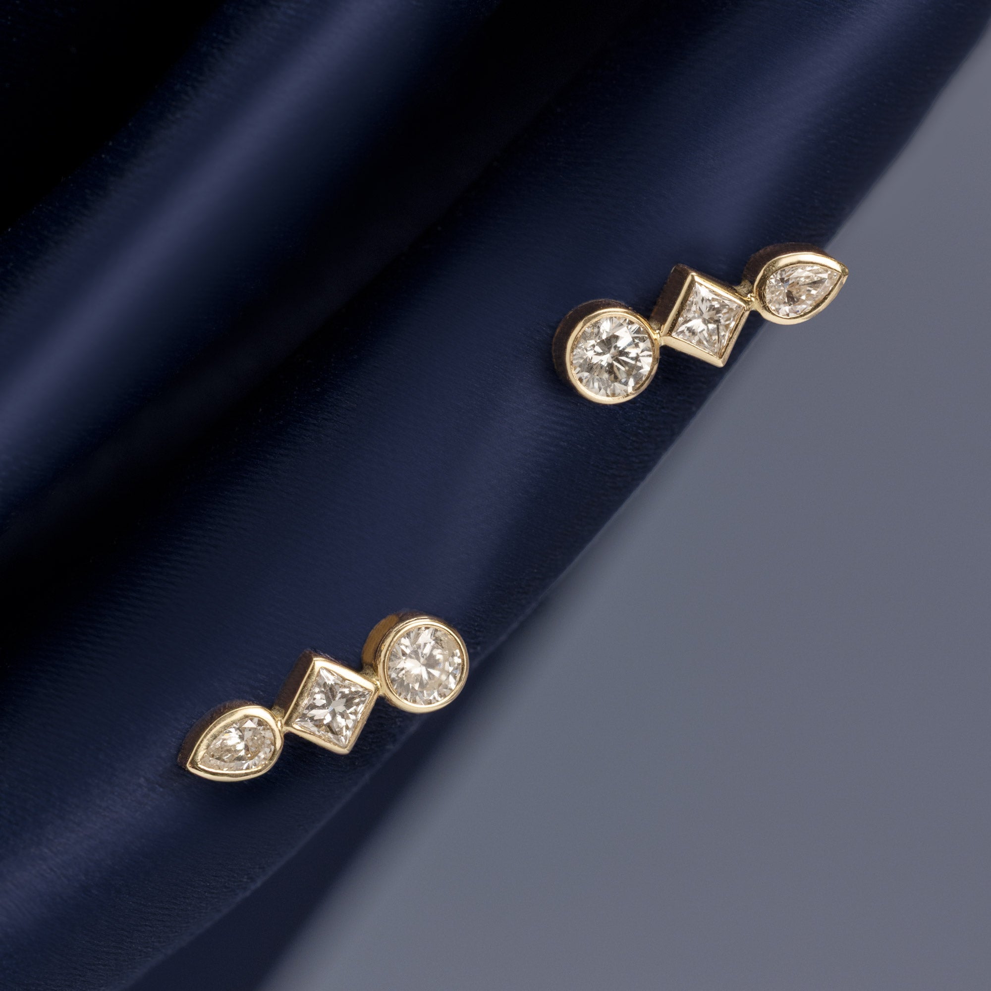 Diamond Squad Ear Climbers in 14K Yellow Gold hanging on navy blue fabric