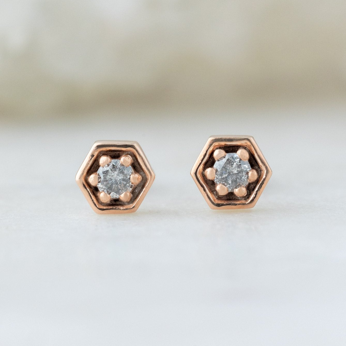 The Galaxy Salt and Pepper Diamond Hexagon Stud Earrings in 14K Rose Gold on White Marble