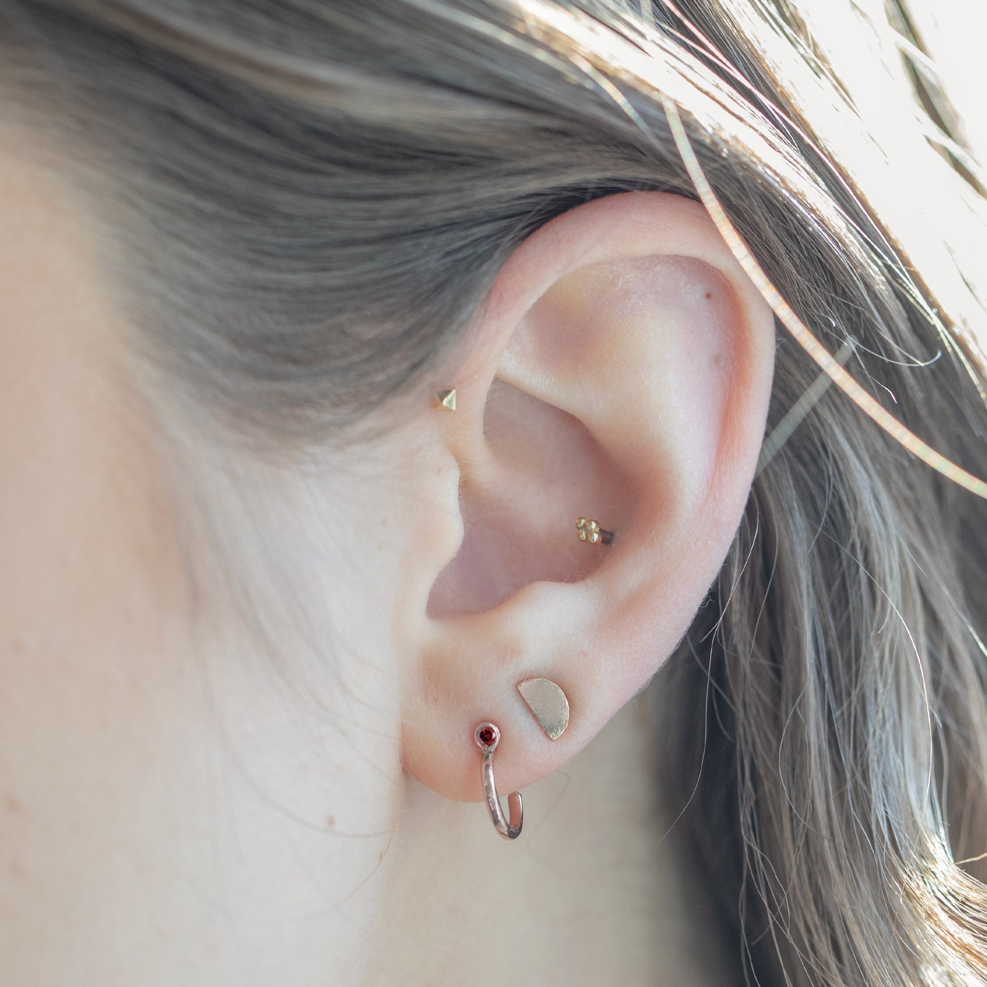 Custom Garnet Birthstone Hoop Earrings | 14K Rose Gold. Displayed on model's ear with additional stud earrings.