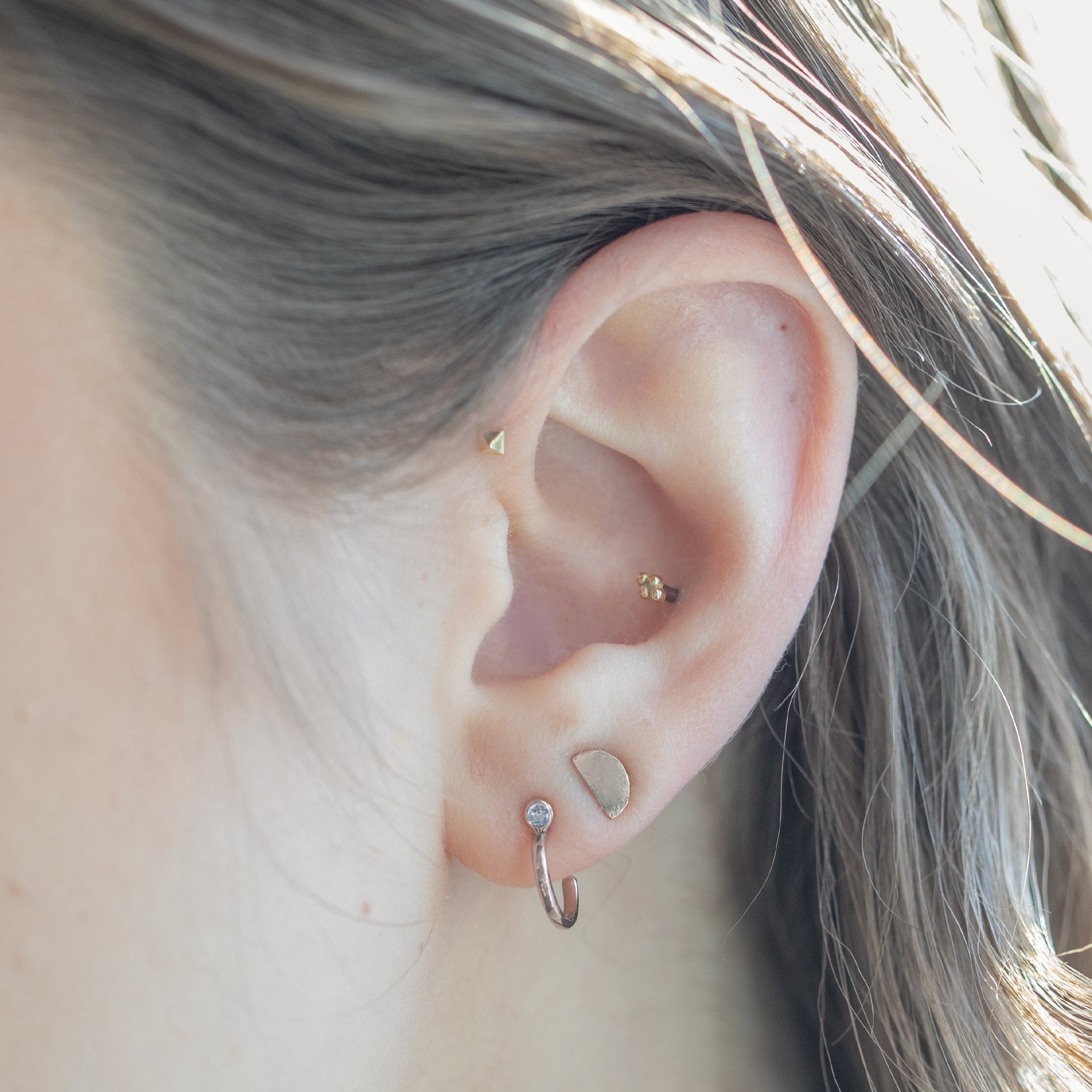 Custom Moonstone Birthstone Hoop Earrings | 14K Rose Gold. Displayed on model's ear with additional stud earrings. 
