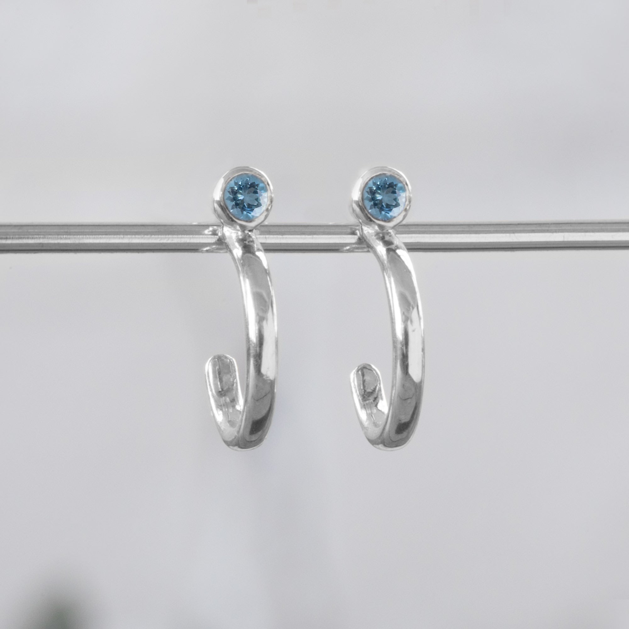 Custom Aquamarine Birthstone Hoop Earrings | 14K White Gold displayed on bar with white blurred background. 