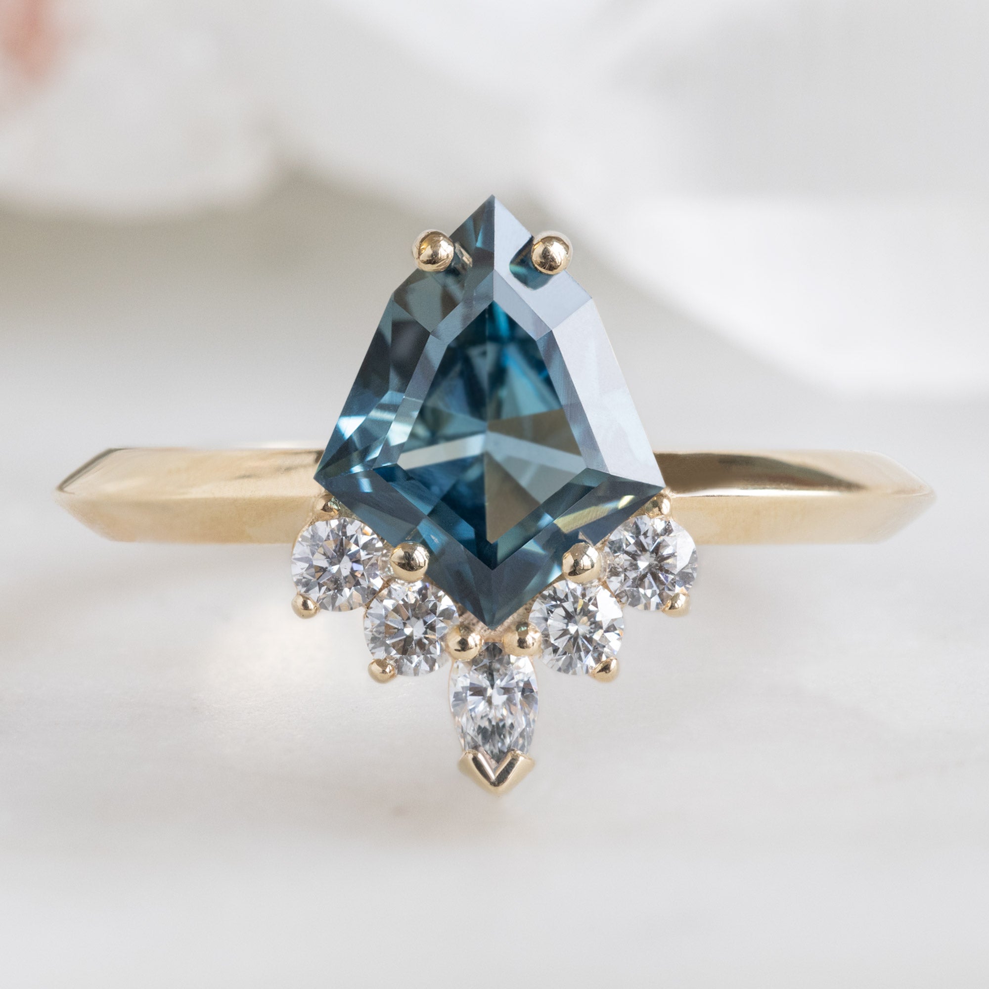 The Aster Ring with a 1.28ct Kite Blue Sapphire in 14K Yellow Gold on White Marble