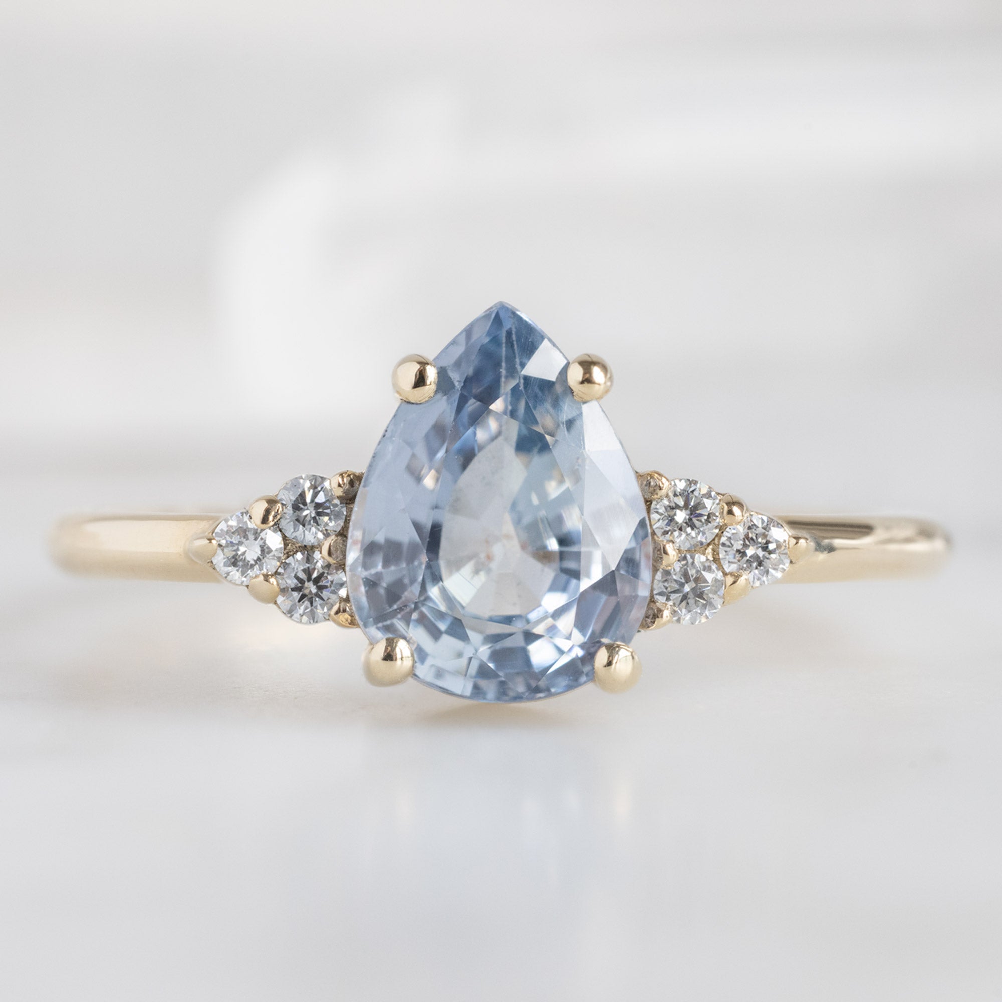 The Ivy Ring | 1.5ct Pear Cut Sapphire in 14K Yellow Gold. Displayed on marble surface. 