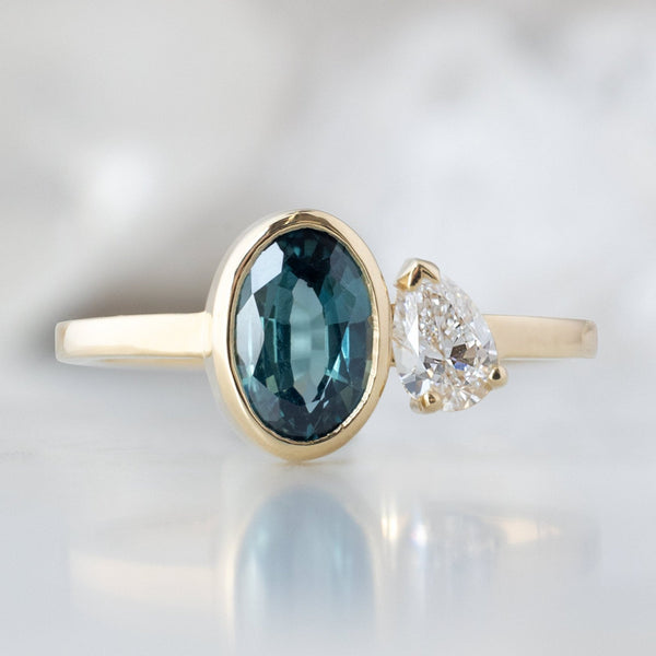 The You and Me Ring with a 1.11ct Oval Cut Sapphire in 14K Yellow Gold on White Marble