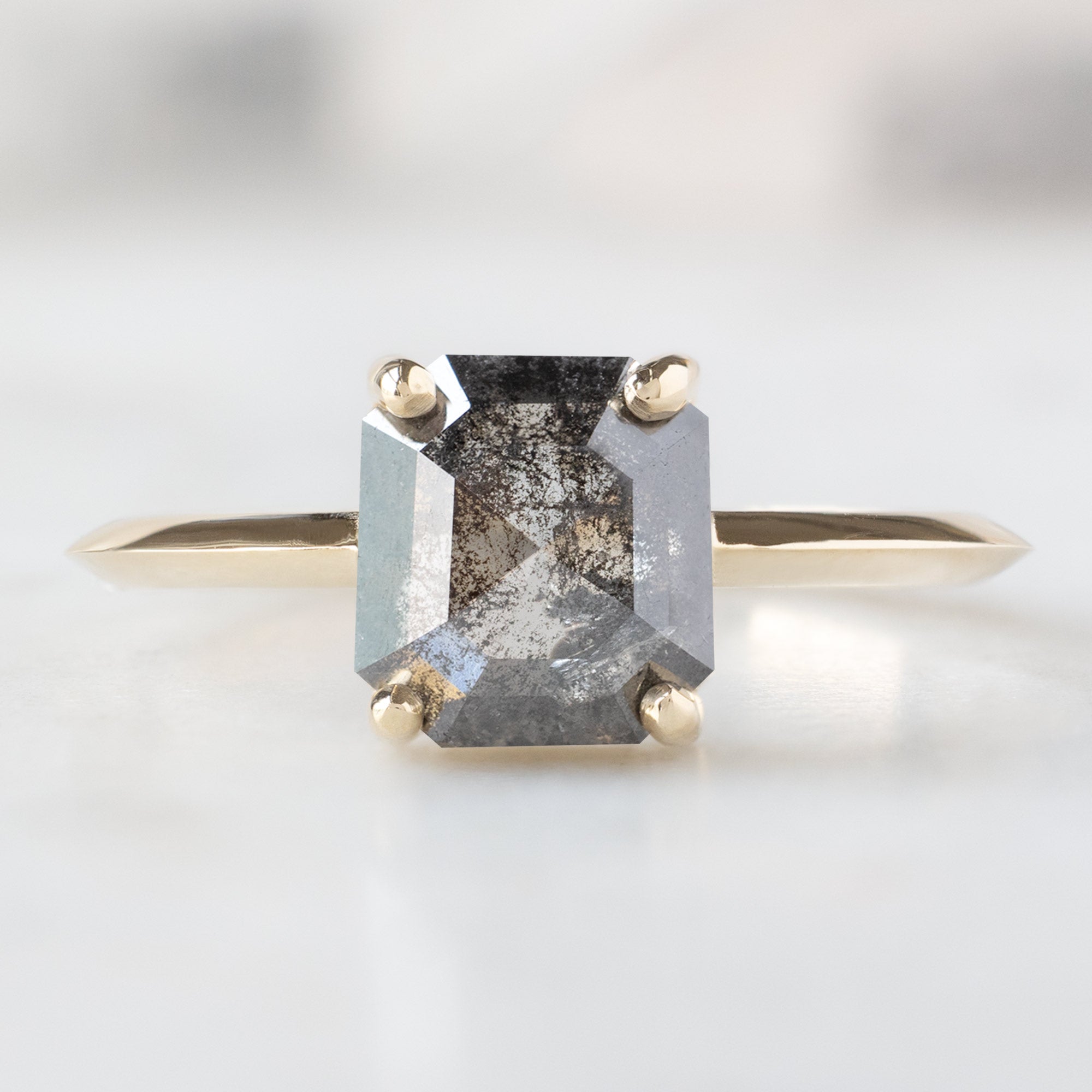 The Bryn Ring with a 1.46ct Emerald Cut Salt and Pepper Diamond in 14K Yellow Gold on White Marble