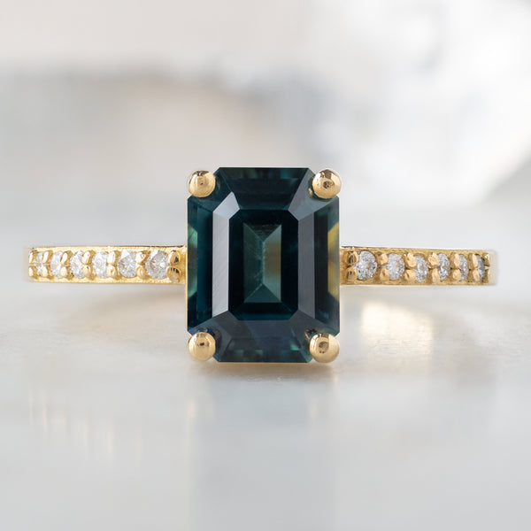 The Willow Ring with a 1.60ct Emerald Cut Teal Sapphire in 18K Yellow Gold on White Marble