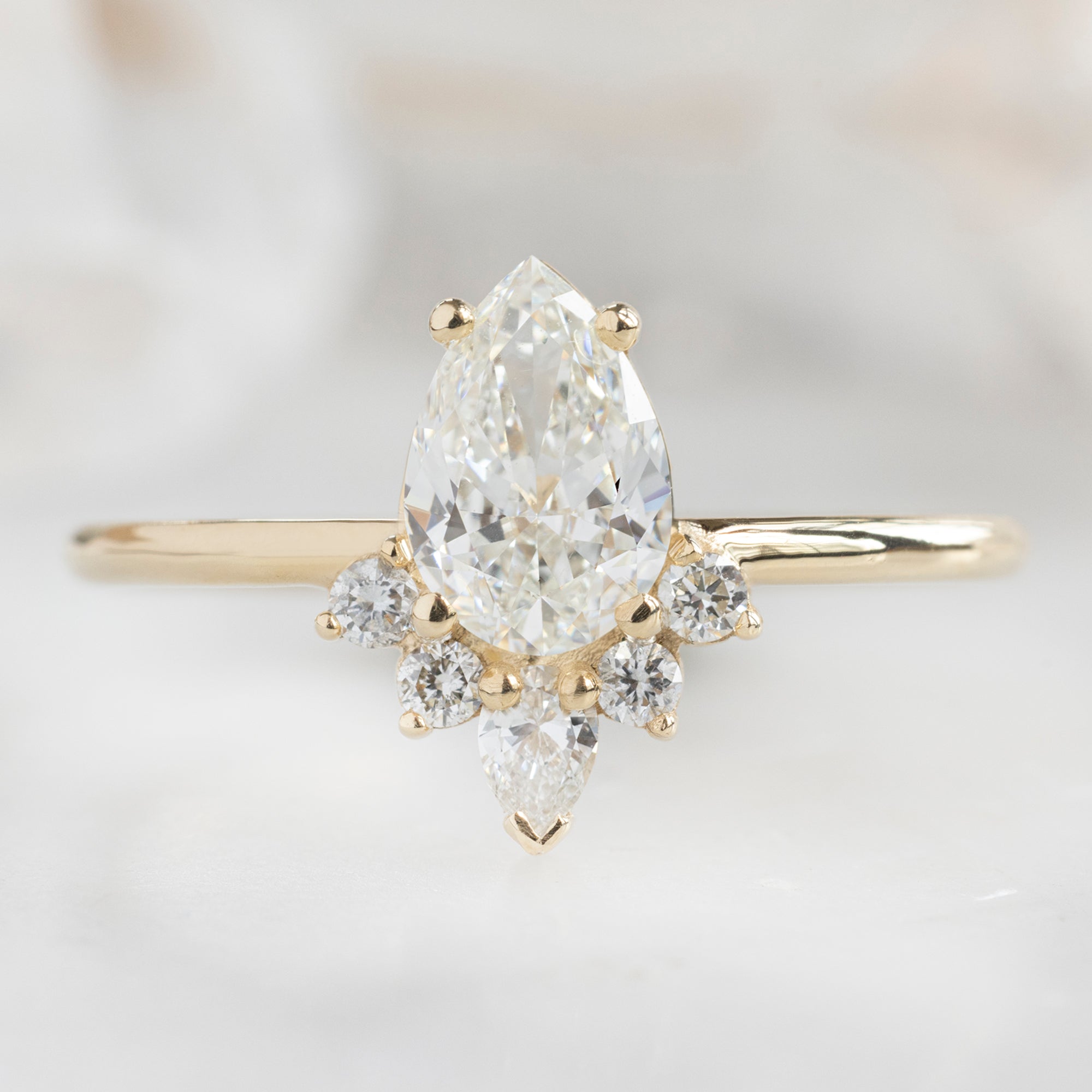 The Aster Ring with a 0.80ct Pear White Diamond in 14K Yellow Gold on White Marble