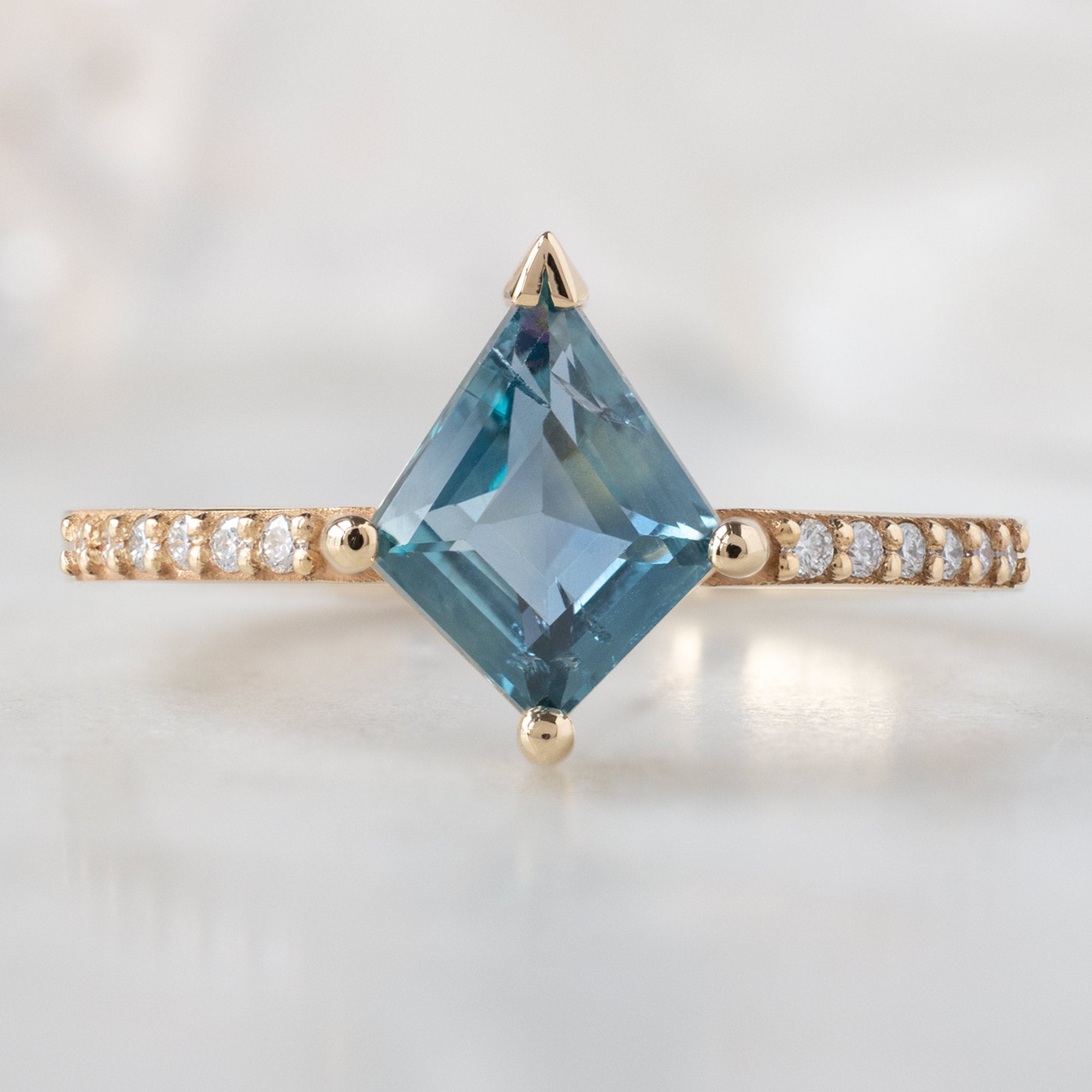 The Willow Ring with a 1.14ct Kite Blue Sapphire in 14K Yellow Gold on White Marble