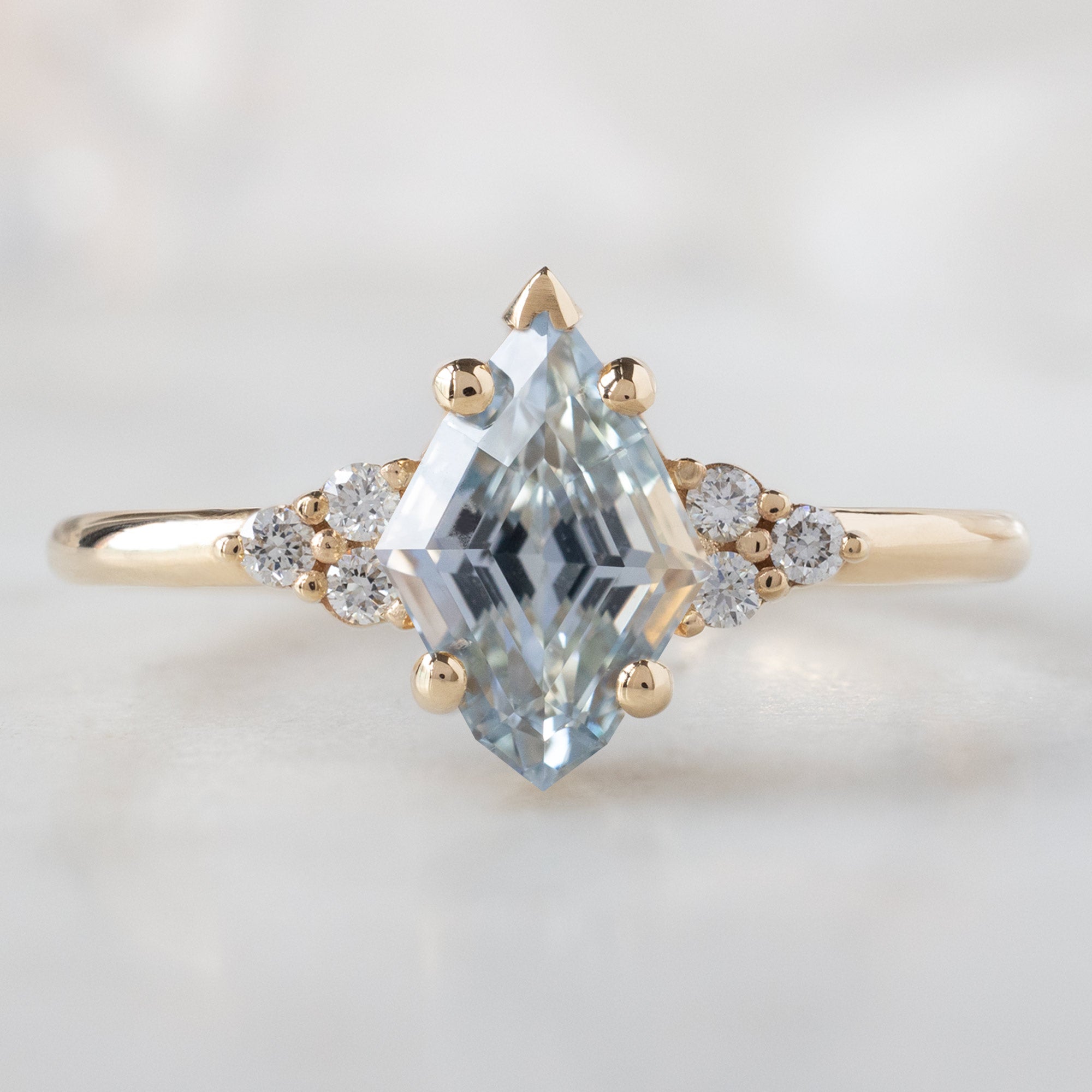 The Ivy Ring with a 1.37ct Kite Blue Sapphire in 14K Yellow Gold on White Marble