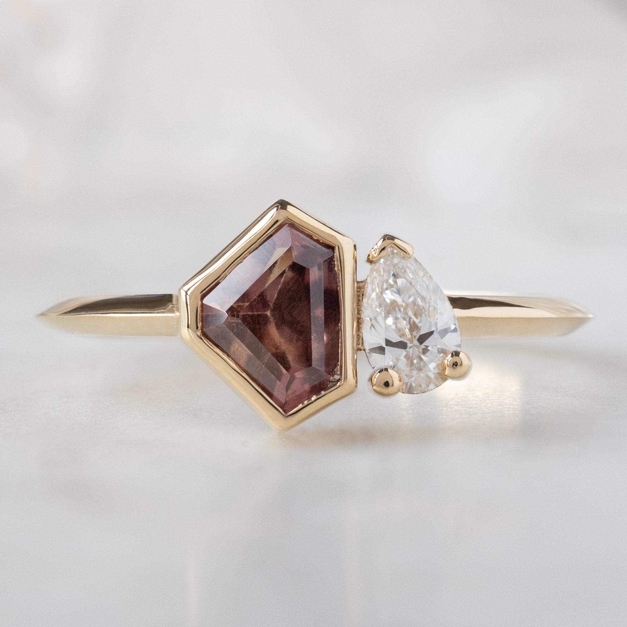 The You & Me Ring with a 0.91ct Shield Orange Sapphire in 14K Yellow Gold on White Marble