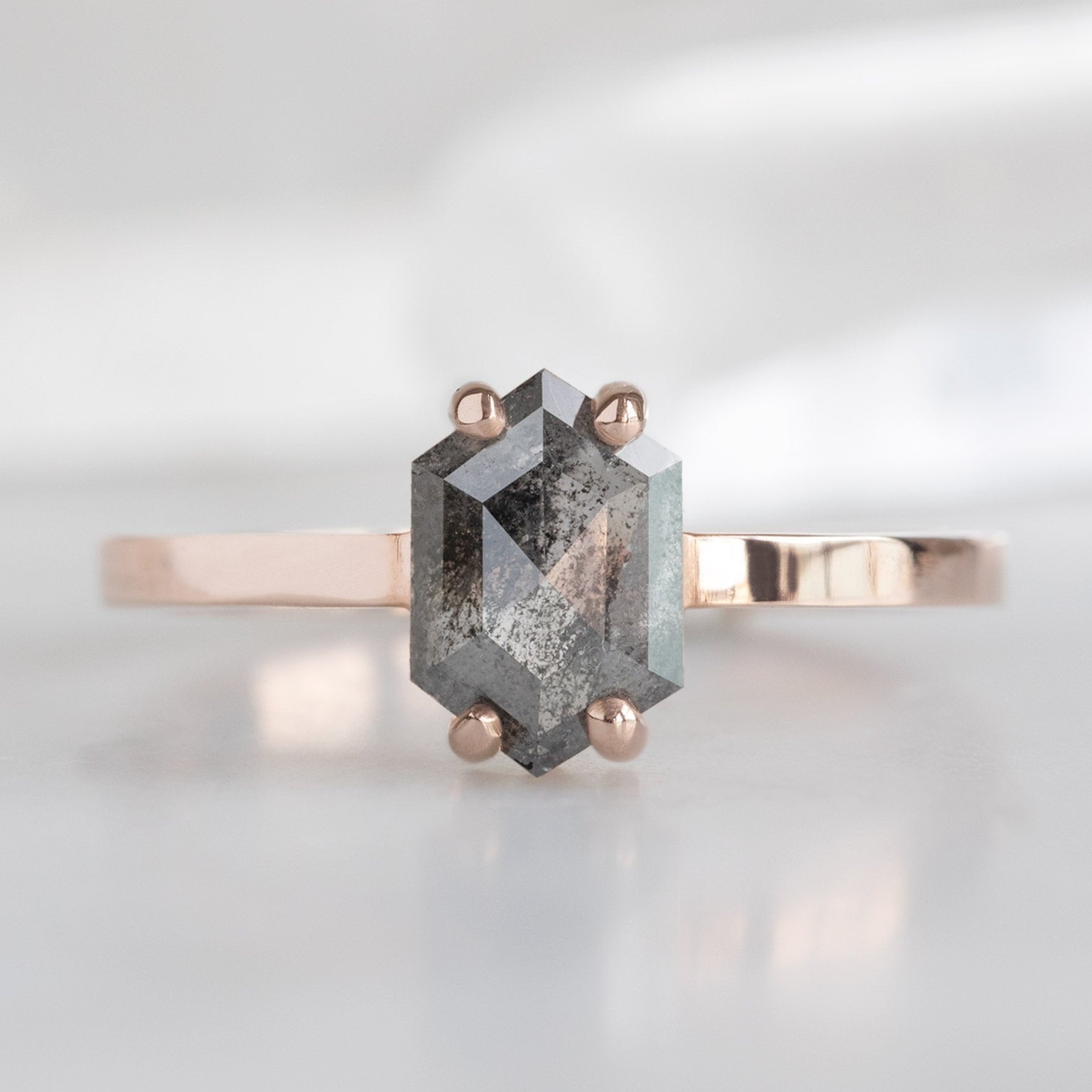 The Bryn Ring with a 0.88 carat Black Hexagon Diamond in 14K Rose Gold displayed on a marble surface. 