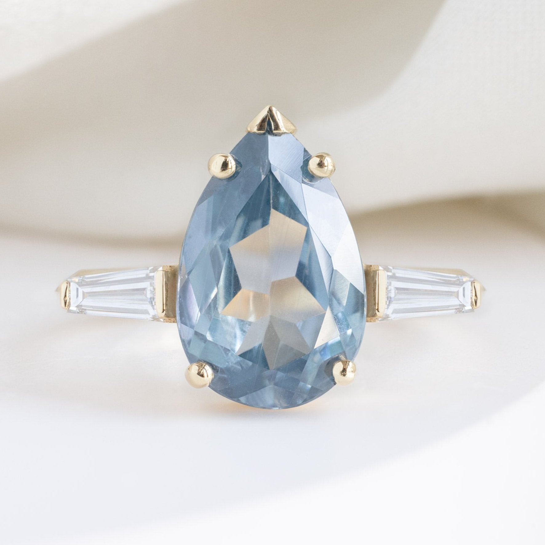 The Ash Luxe with a 3.62ct Pear Cut Sapphire in 18K Yellow Gold on White Marble