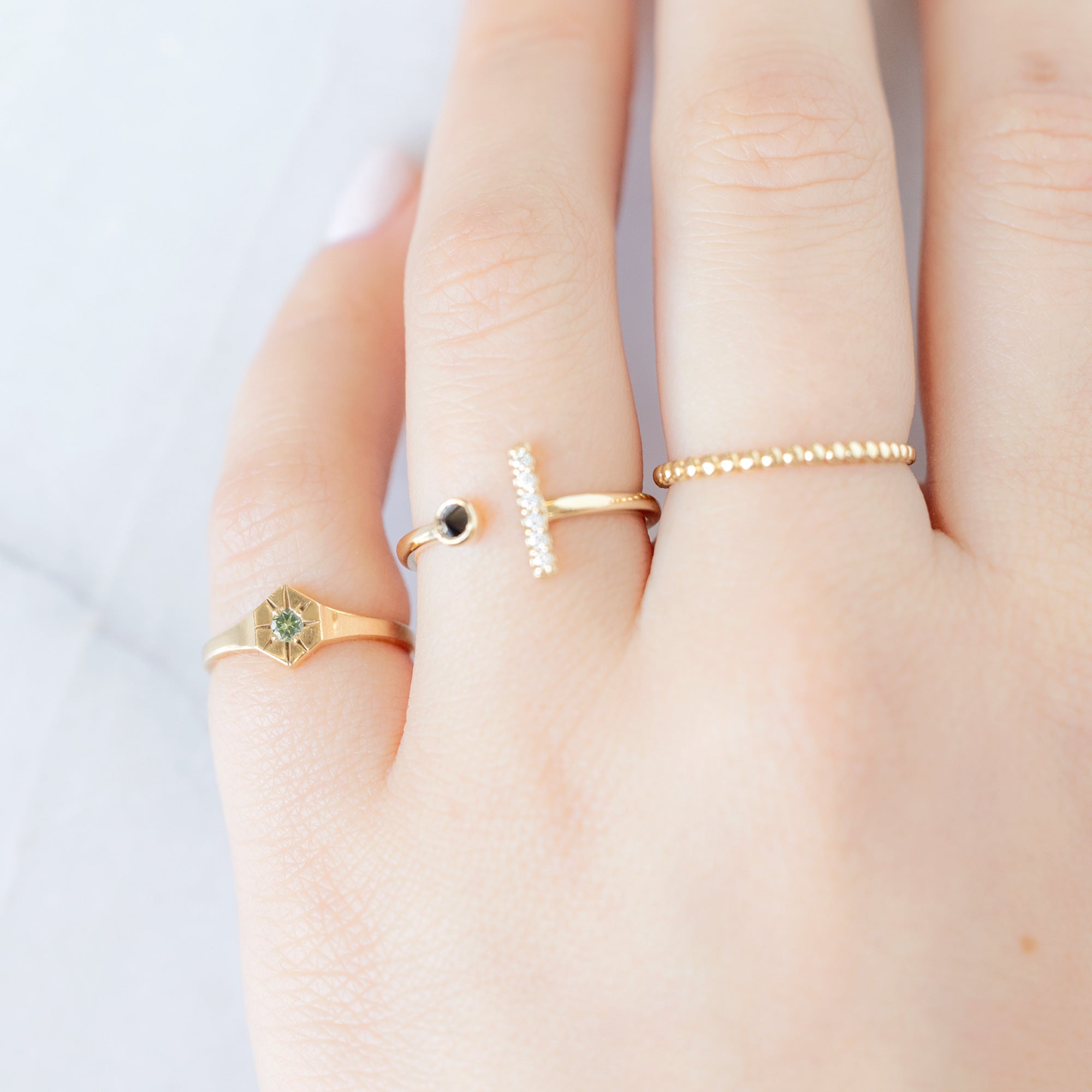 Custom Peridot Birthstone Signet Ring | 10K Yellow Gold. Displayed on model's left hand pinky finger alongside two other rings on consecutive fingers. 