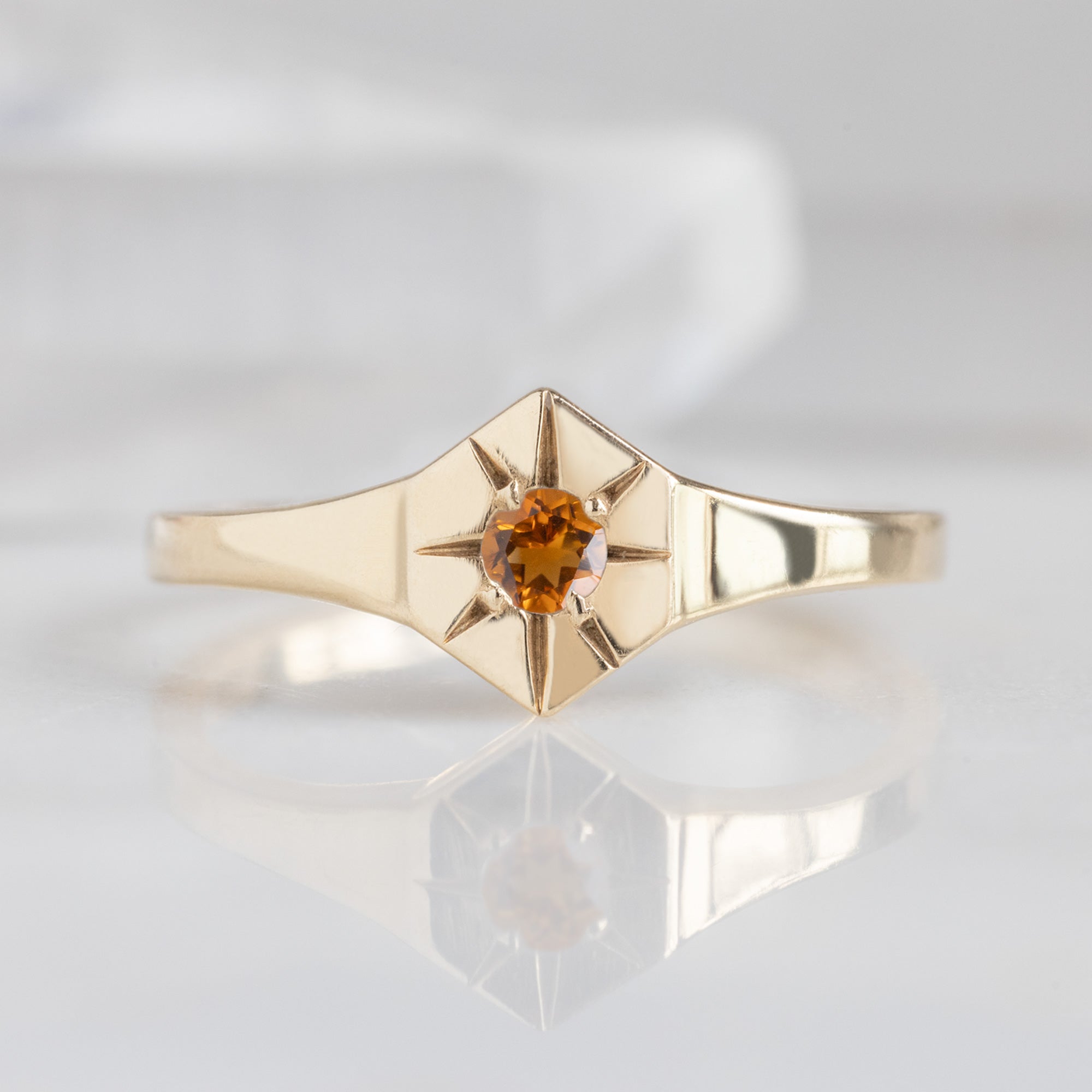 Custom Citrine Birthstone Signet Ring | 10K Yellow Gold displayed on marble surface with white blurred background. 