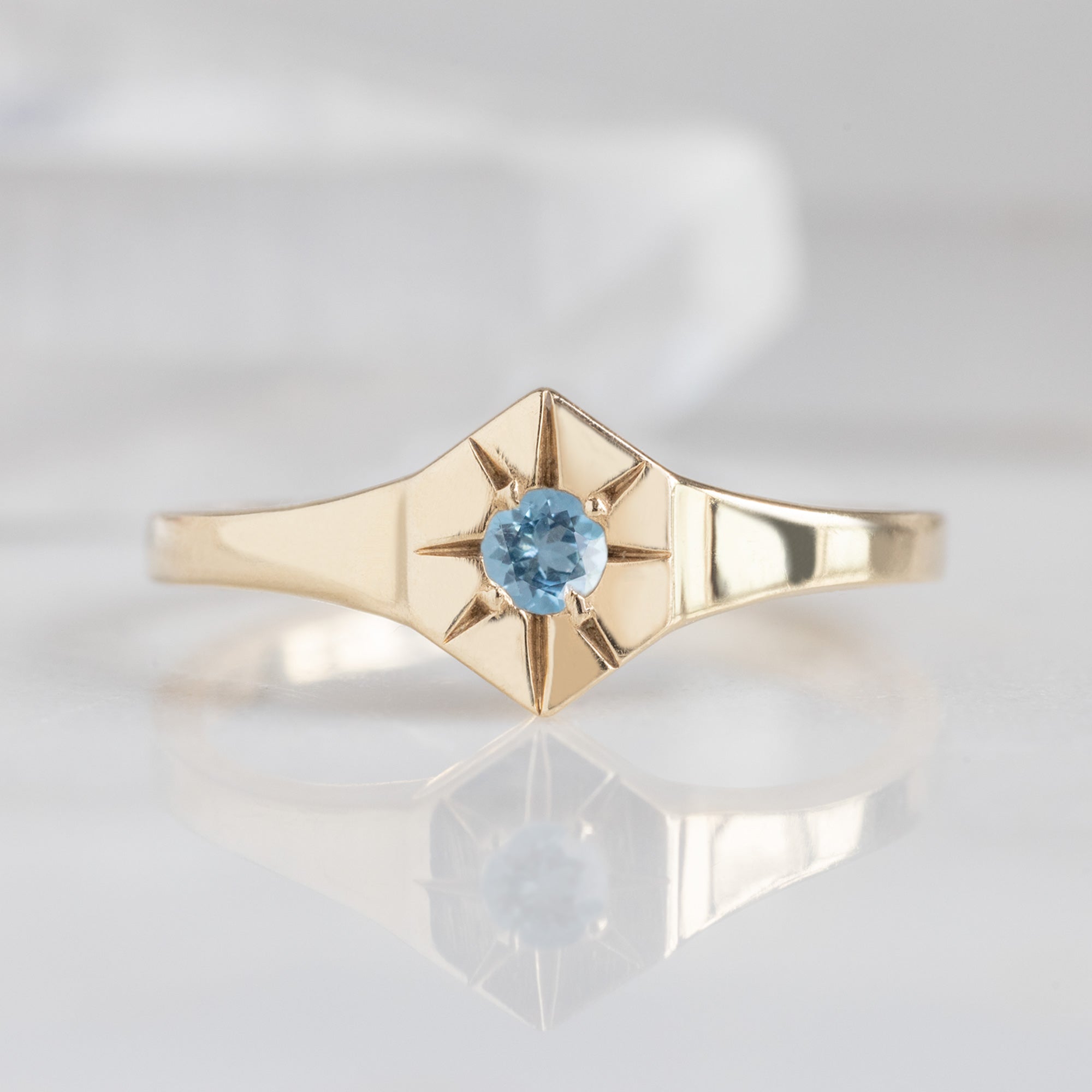 Custom Aquamarine Birthstone Signet Ring | 10K Yellow Gold displayed on marble surface with white blurred background. 
