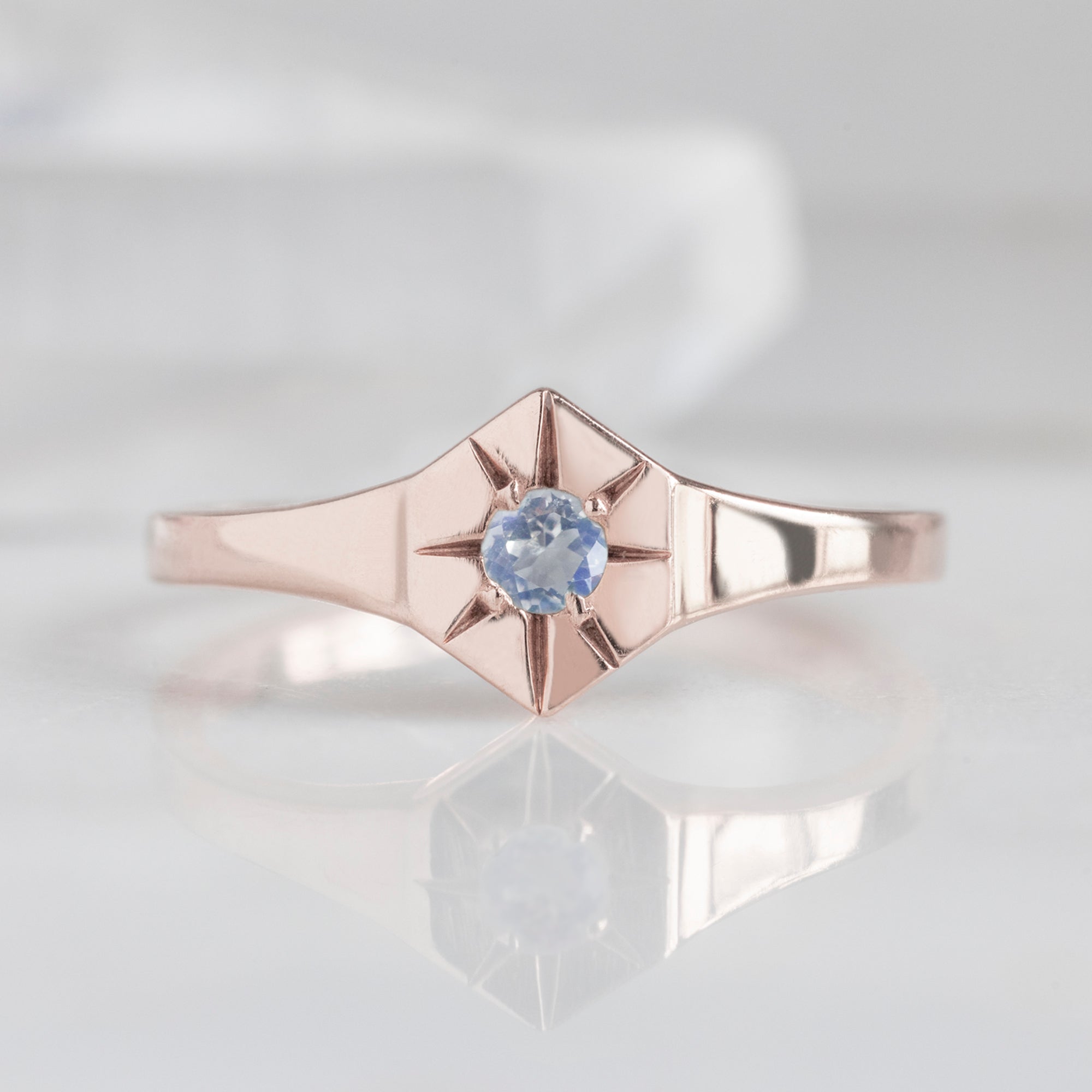 Custom Moonstone Birthstone Signet Ring | 10K Rose Gold. Displayed on marble surface with blurred background. 