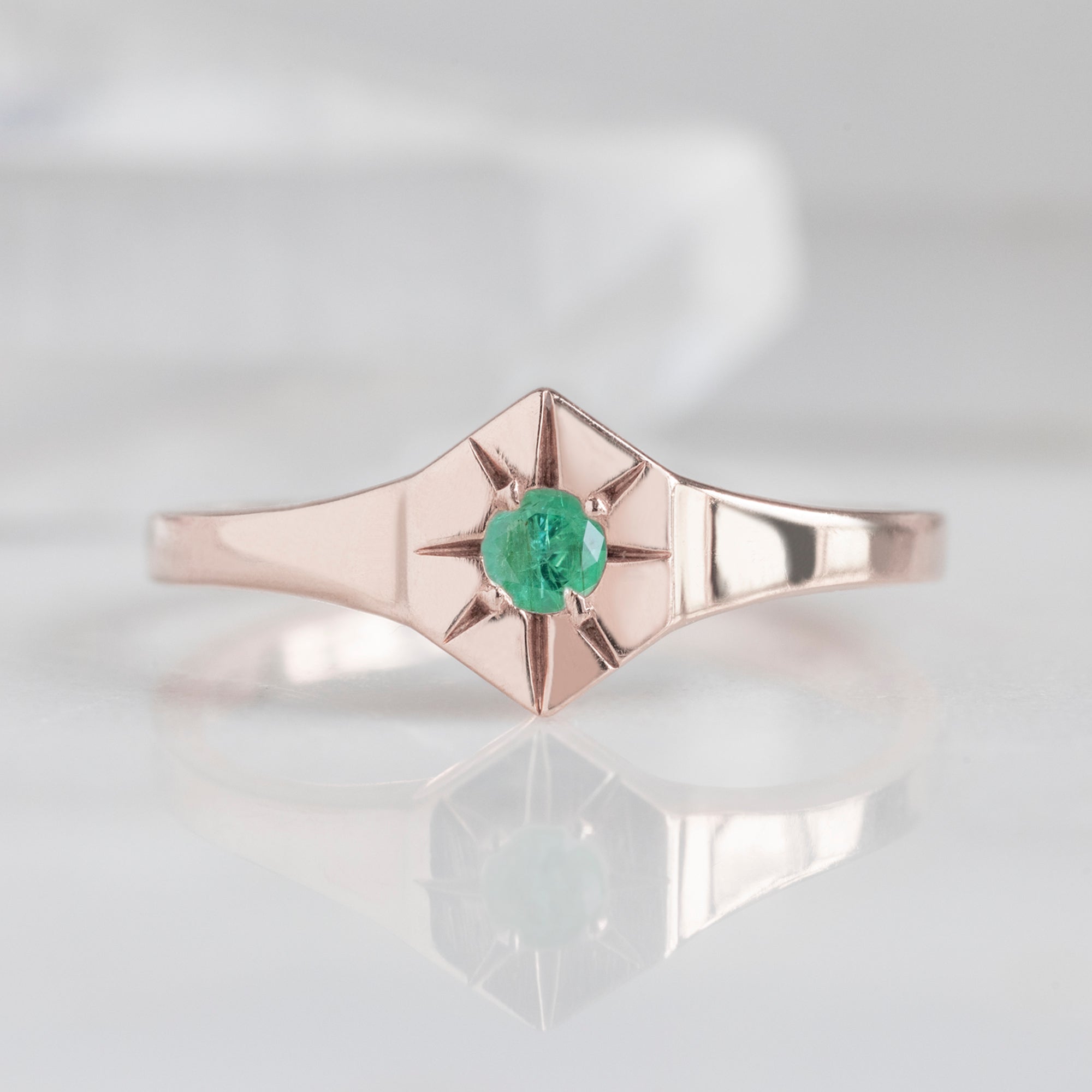 Custom Emerald Birthstone Signet Ring | 10K Rose Gold. Displayed on marble surface with white blurred background.