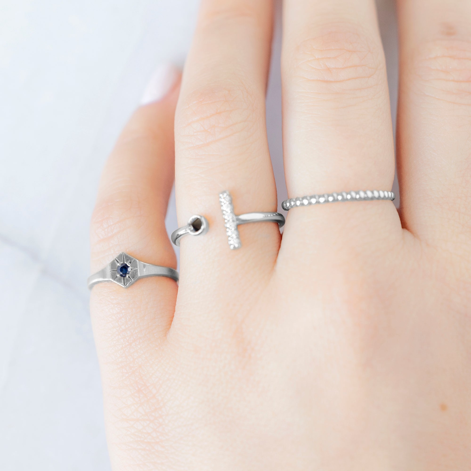 Custom Blue Sapphire Birthstone Signet Ring | 10K White Gold displayed on model's left hand pinky finger alongside two other rings on consecutive fingers. 