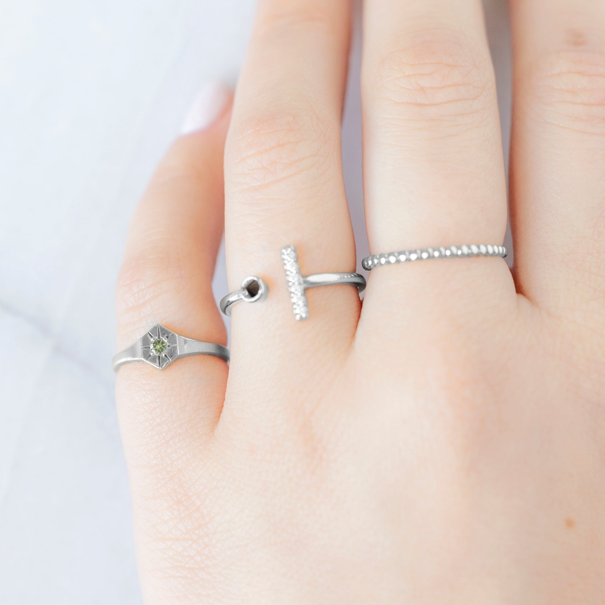 Custom Peridot Birthstone Signet Ring | 10K White Gold. Displayed on model's left hand pinky finger alongside two other rings on consecutive fingers.