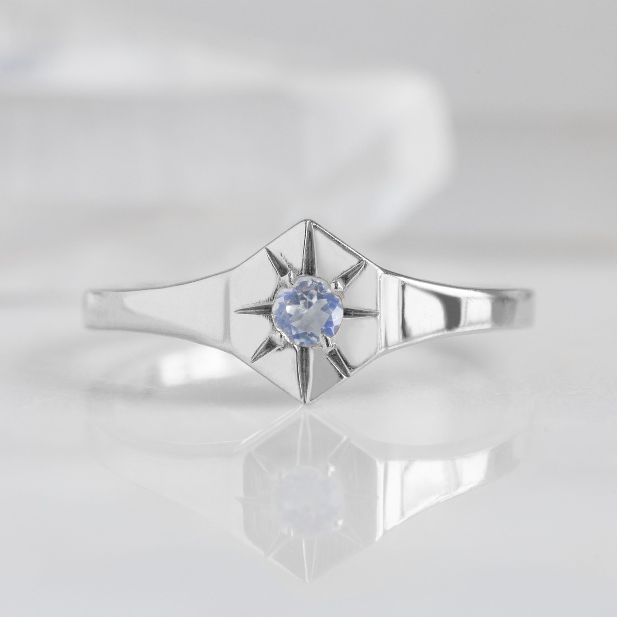 Custom Moonstone Birthstone Signet Ring | 10K White Gold. Displayed on marble surface with white blurred background. 