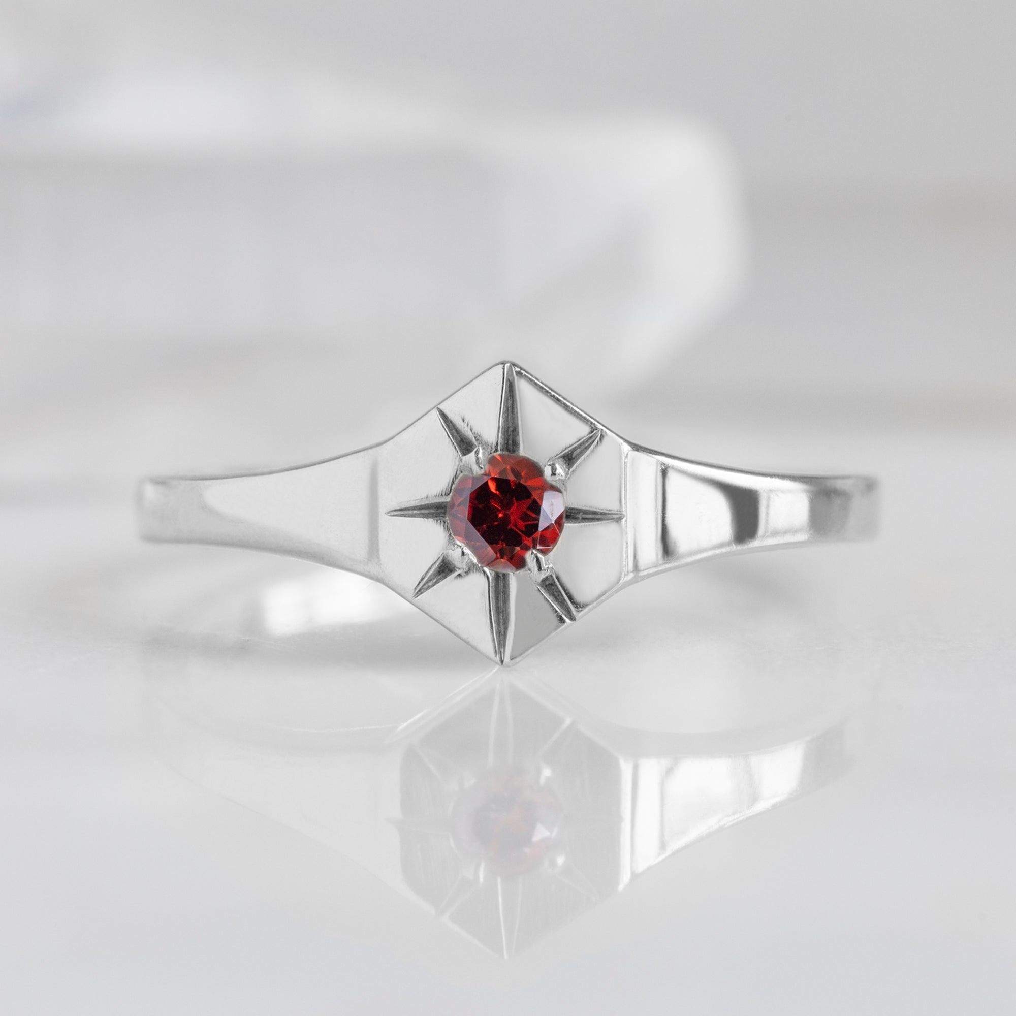 Custom Garnet Birthstone Signet Ring | 10K White Gold. Displayed on marble surface with white blurred background. 