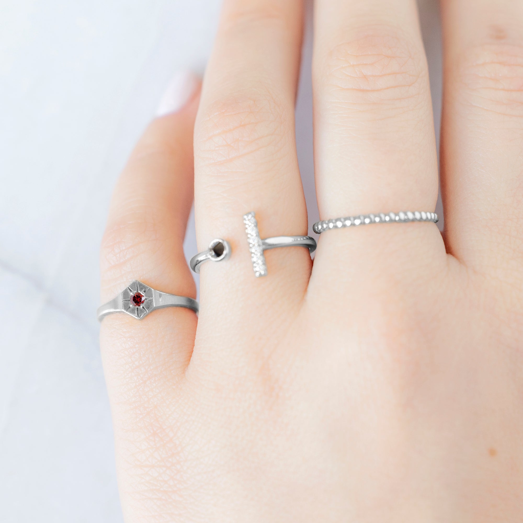 Custom Garnet Birthstone Signet Ring | 10K White Gold. Displayed on model's left hand pinky finger, alongside two other rings on consecutive fingers. 