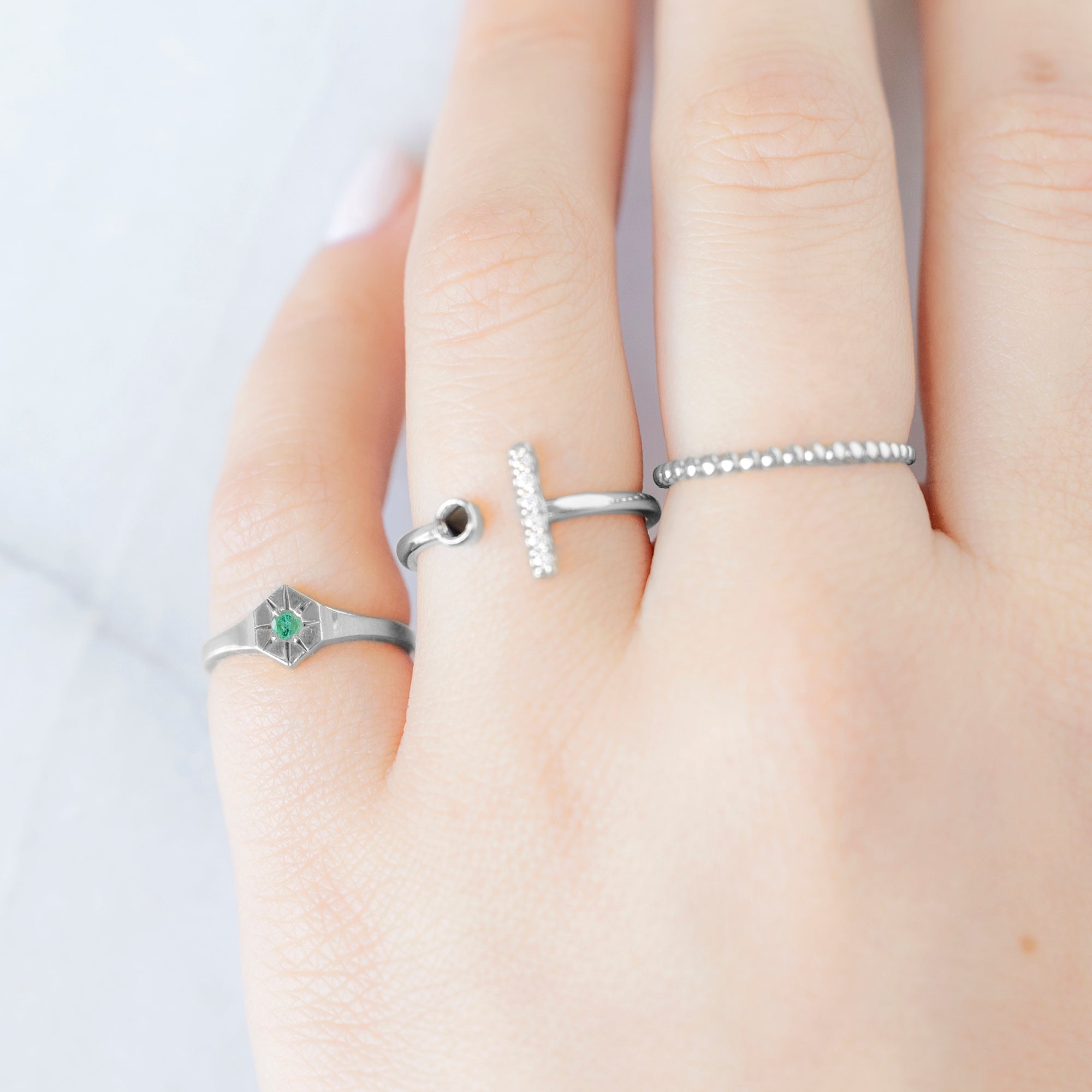 Custom Emerald Birthstone Signet Ring | 10K White Gold. Displayed on model's left hand pinky finger alongside two other rings on consecutive fingers.