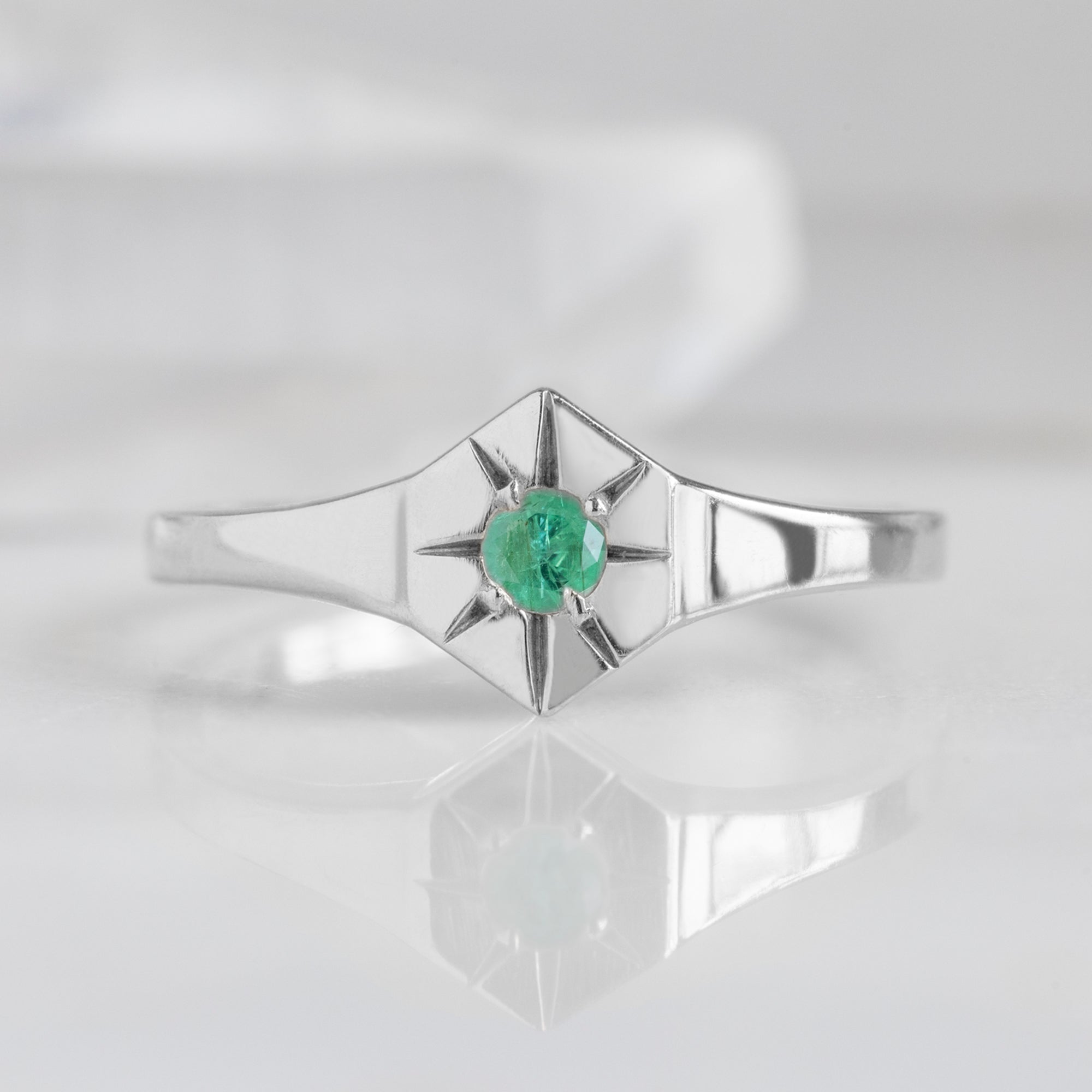 Custom Emerald Birthstone Signet Ring | 10K White Gold. Displayed on marble surface with white blurred background. 