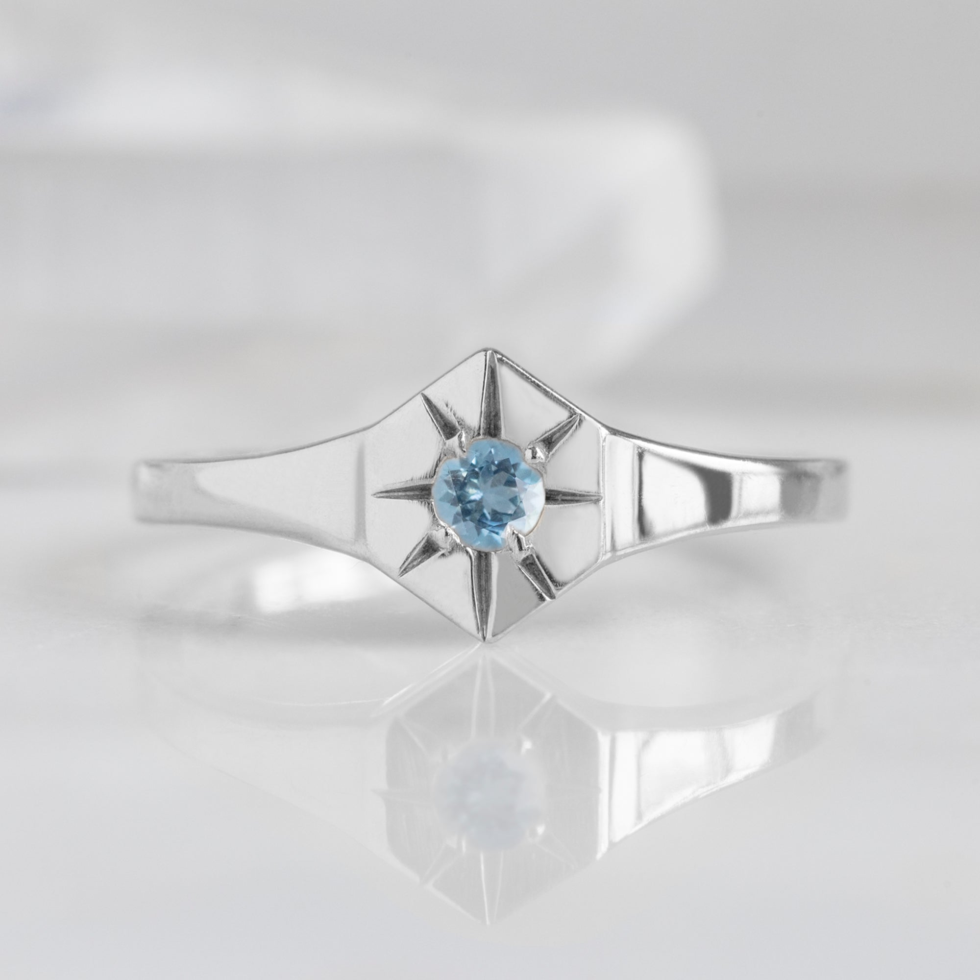 Custom Aquamarine Birthstone Signet Ring | 10K White Gold displayed on marble surface with white blurred background.