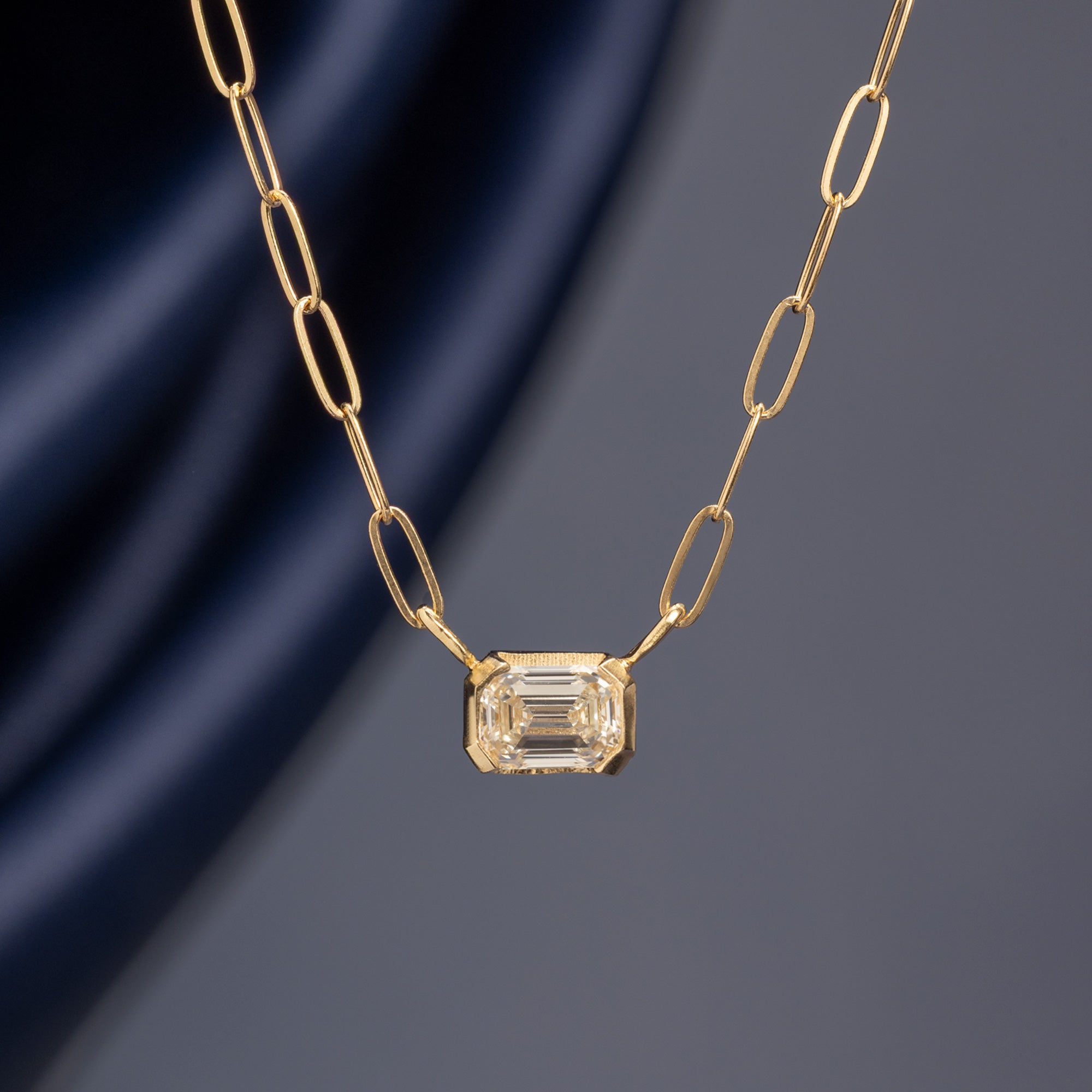 Deco Diamond Solitaire Necklace in 10K Yellow Gold hanging on muted blue background