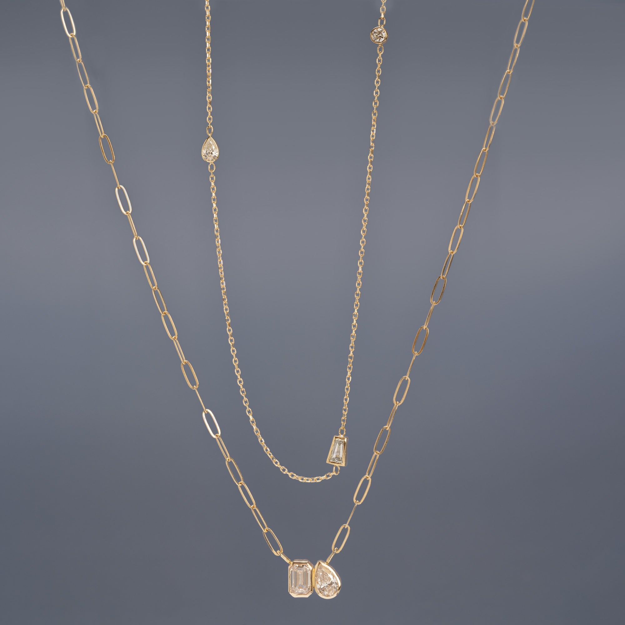 The You and Me Diamond Necklace and Baguette Diamond Chain Necklace in 10K Yellow Gold hanging in front of muted blue background