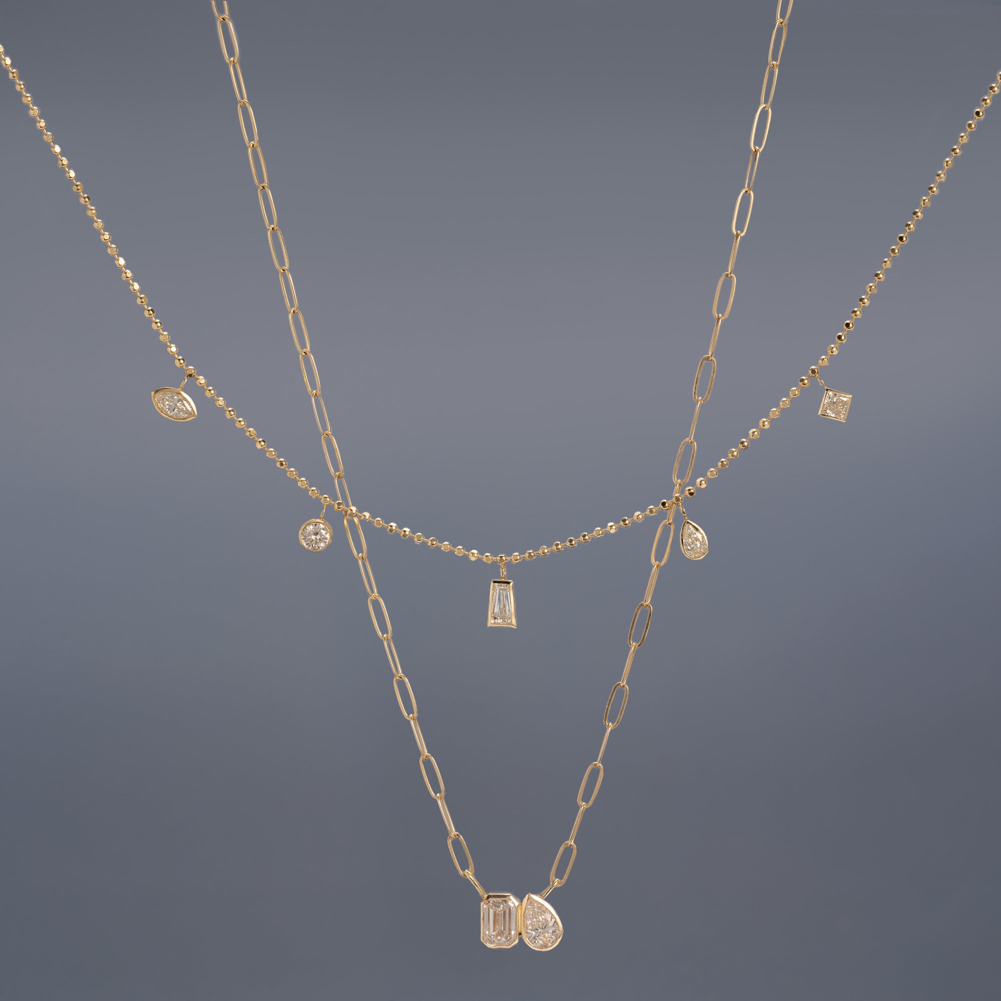 The You and Me Diamond Necklace and Diamond Pennant Necklace in 10K Yellow Gold hanging in front of muted blue background