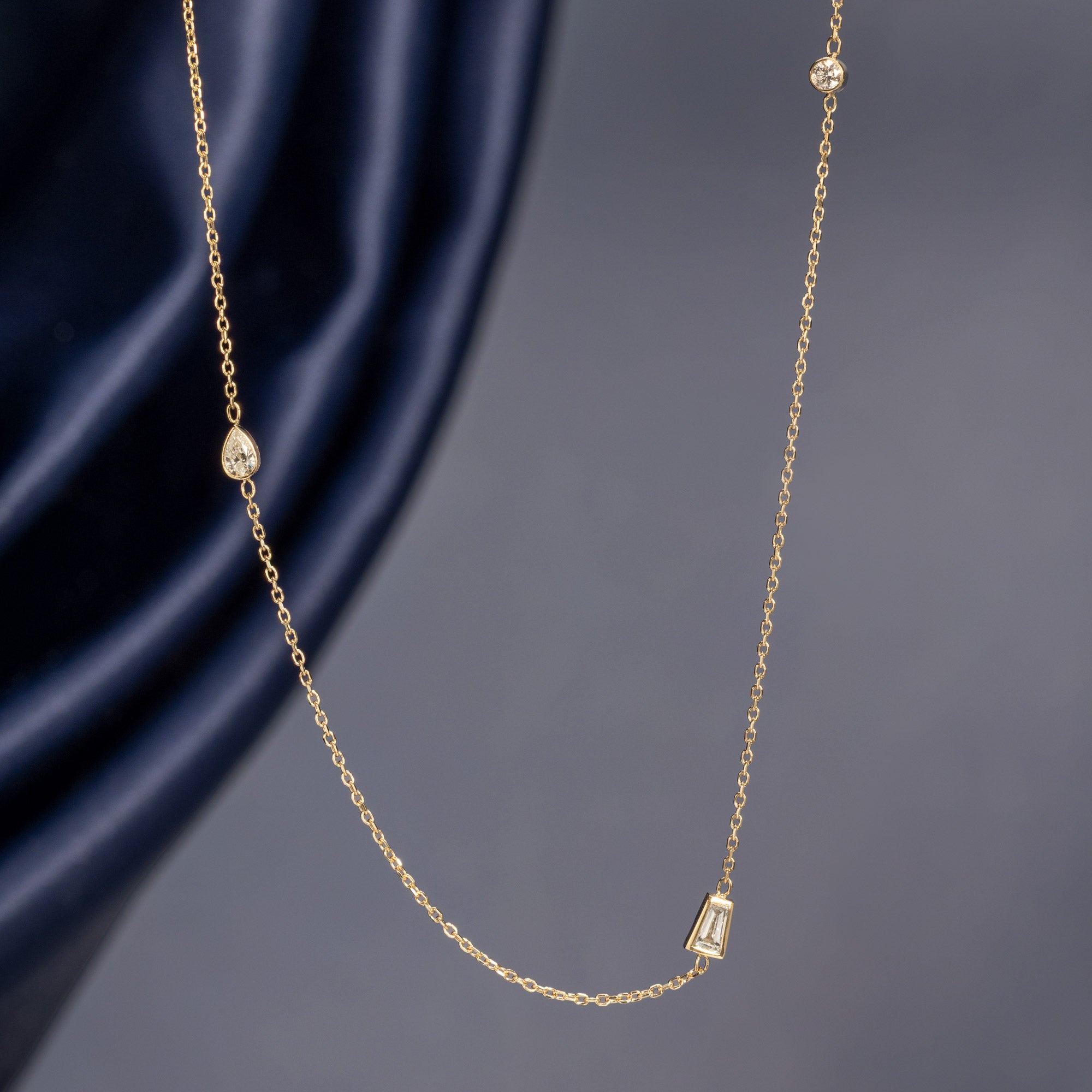 Baguette Diamond Chain Necklace in 10K Yellow Gold hanging in front of muted blue background