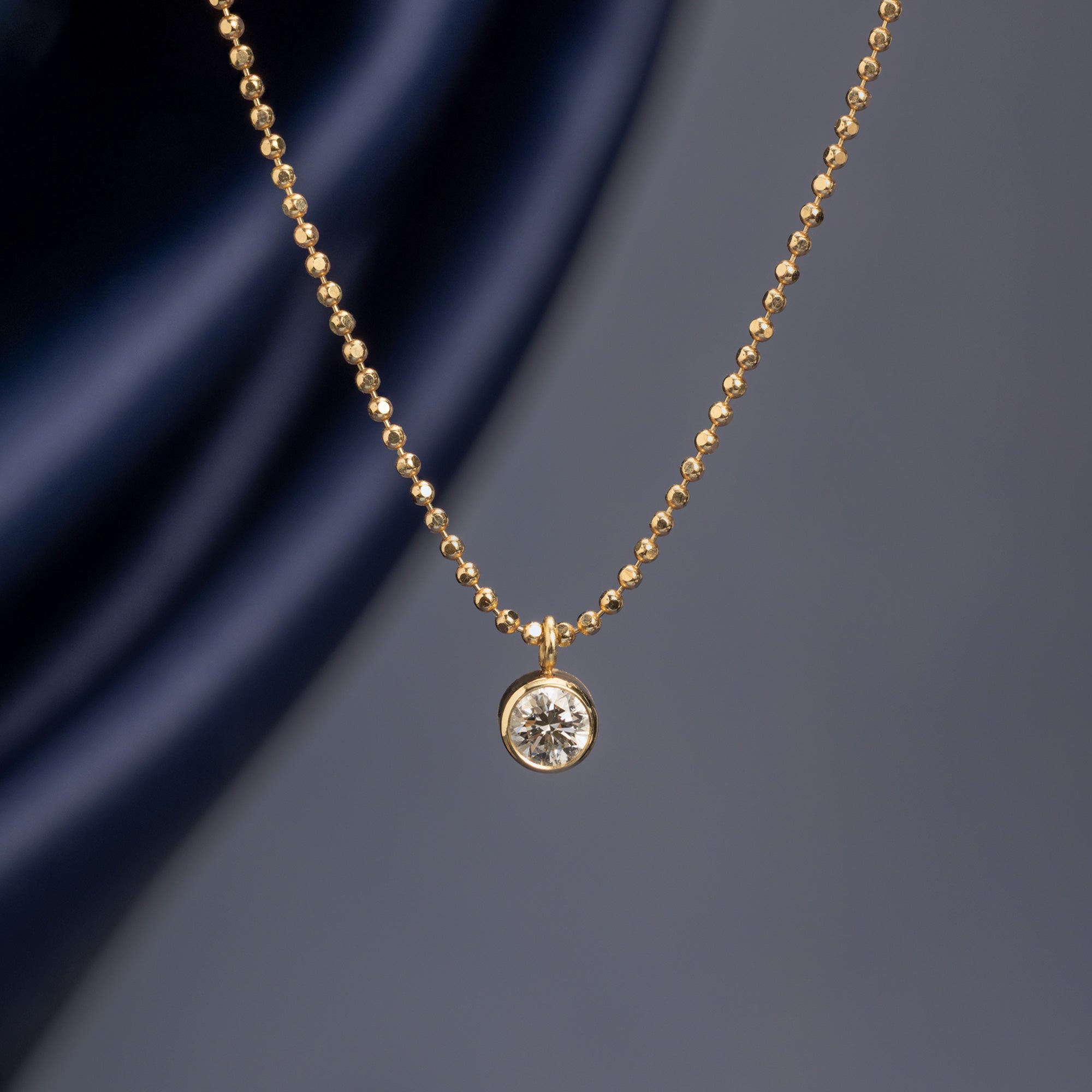 ‘Not Your Typical Solitaire’ Diamond Necklace in 10K Yellow Gold hanging in front of muted blue background