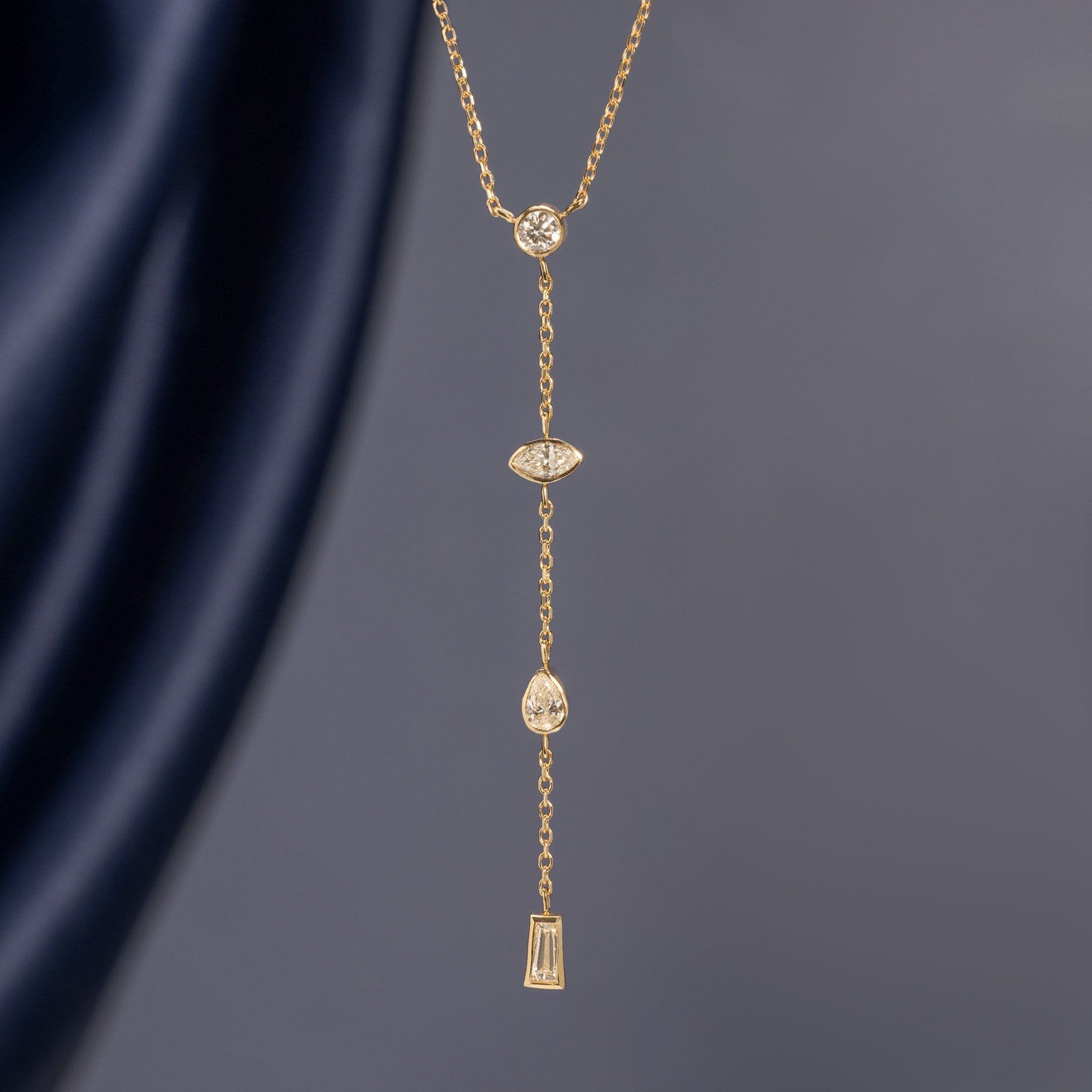 ‘Date Night’ Diamond Lariat Necklace in 10K Yellow Gold hanging in front of muted blue background