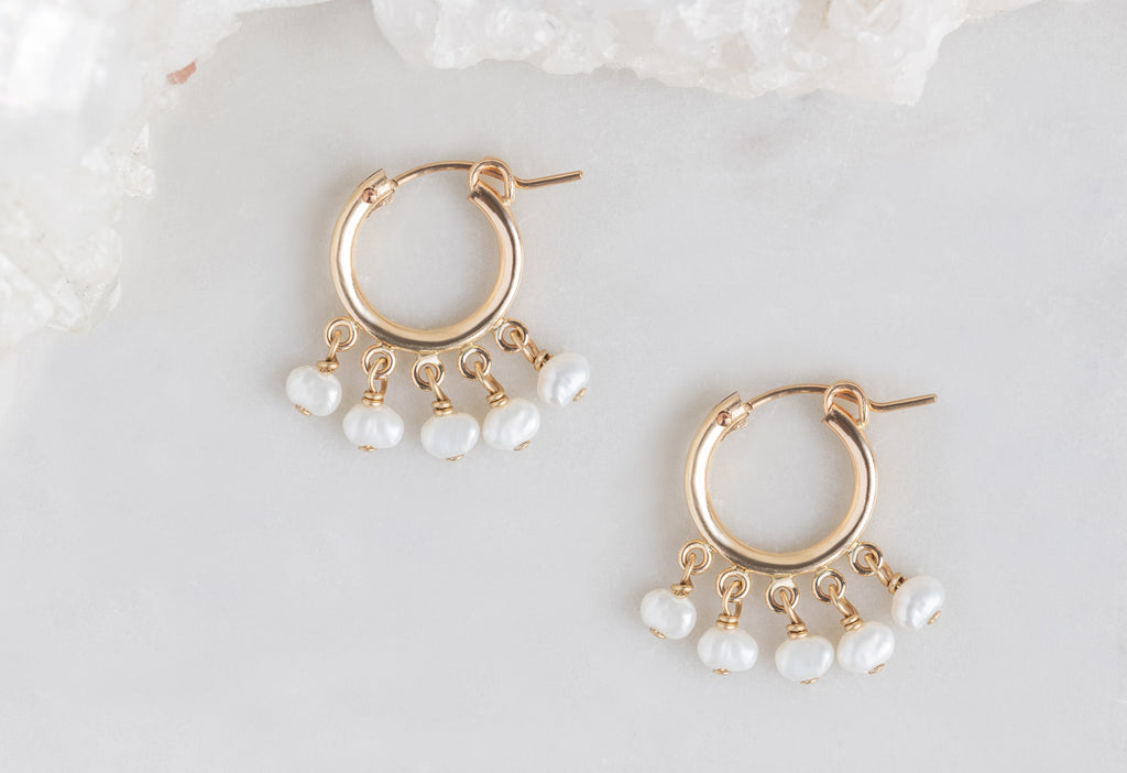 Pearl Party Hoop Earrings lying flat on white marble tile