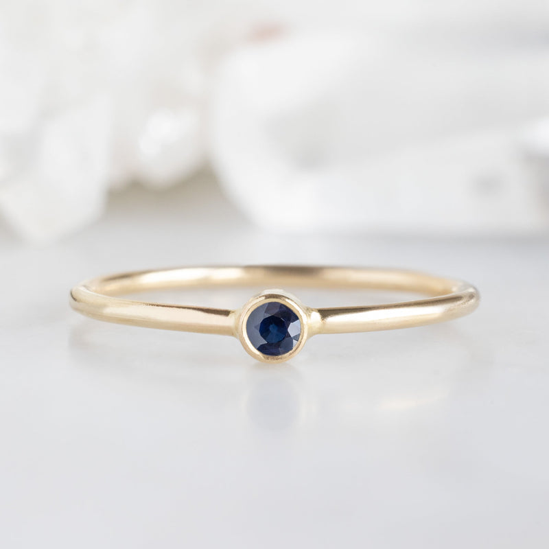 Custom Blue Sapphire Birthstone Stacking Ring | 10K Yellow Gold displayed on marble surface with white blurred background. 