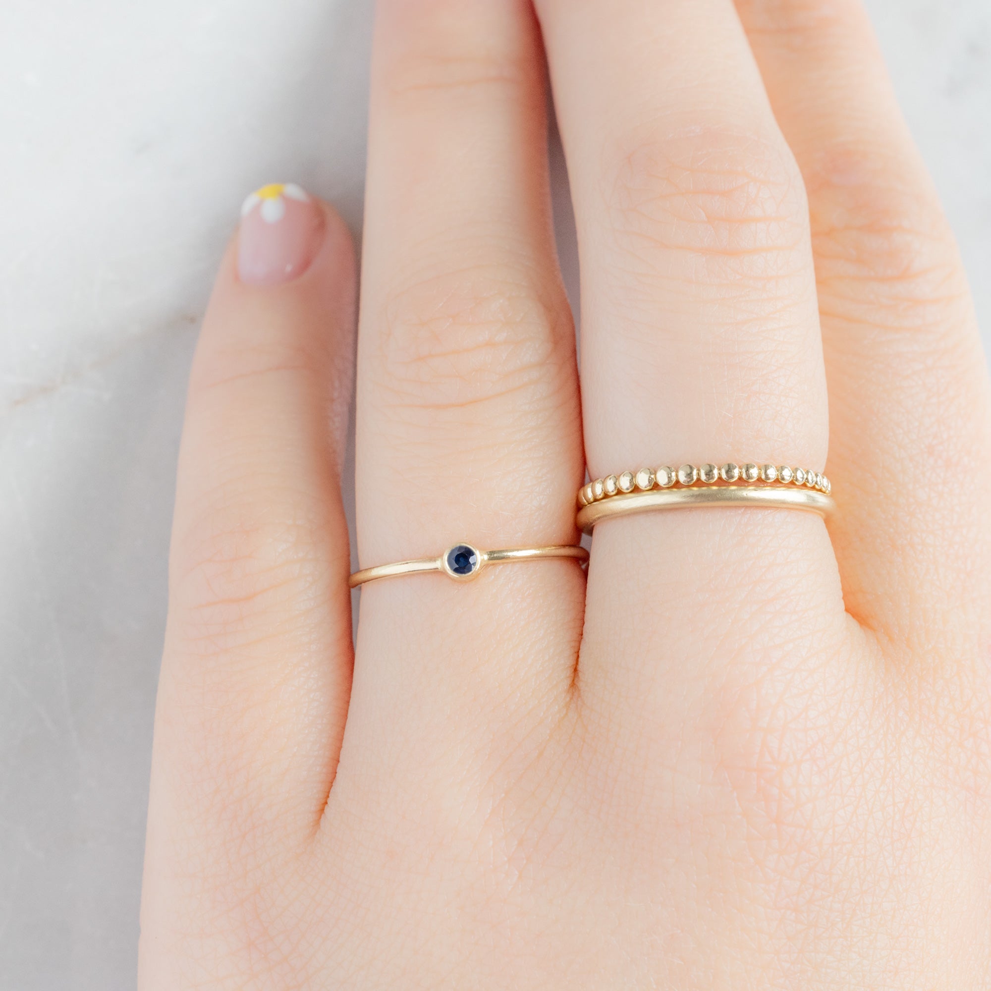 Custom Blue Sapphire Birthstone Stacking Ring | 10K Yellow Gold displayed on model's left hand ring finger alongside two other rings on consecutive finger. 