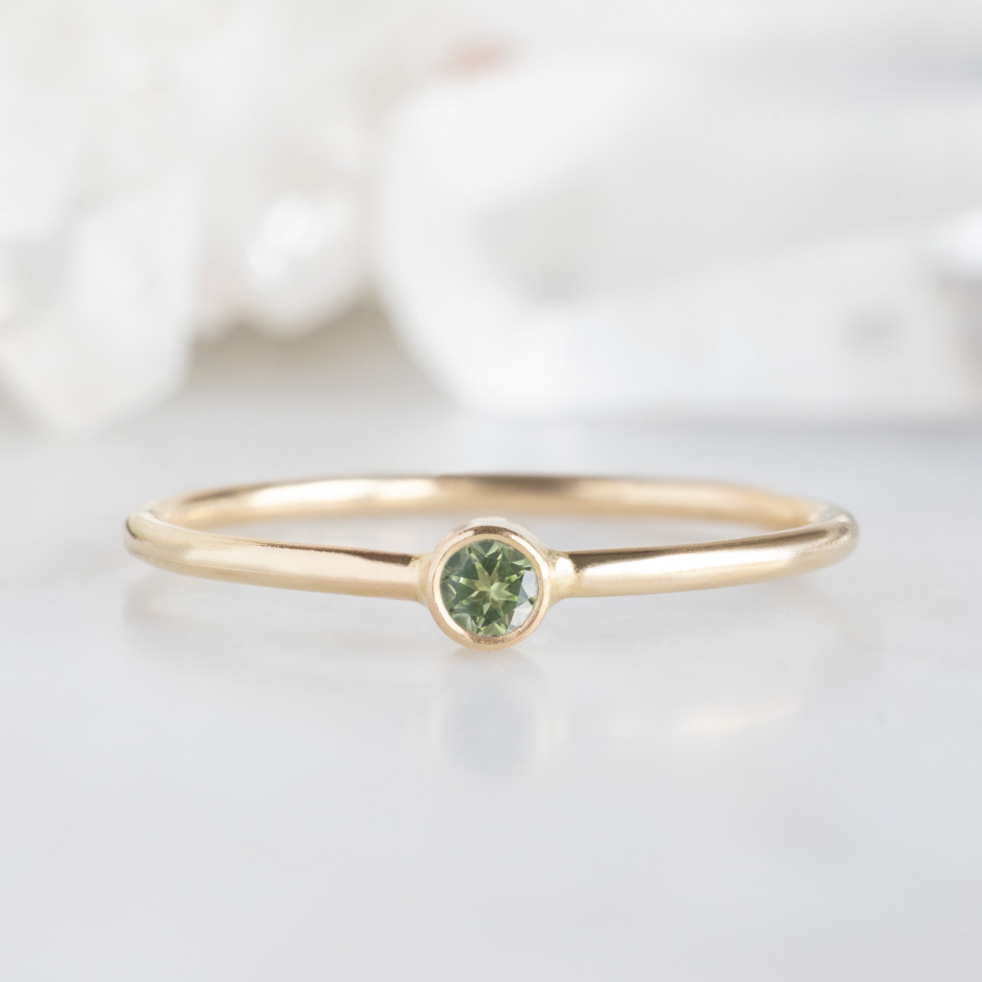 Custom Peridot Birthstone Stacking Ring | 10K Yellow Gold. Displayed on marble surface with white blurred background.
