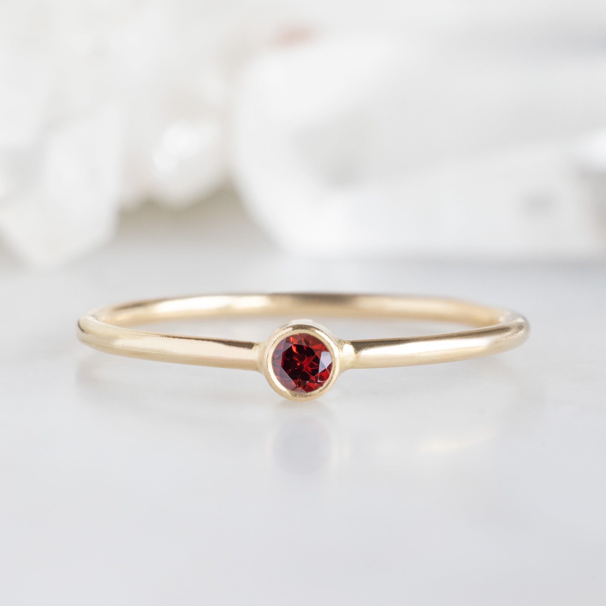 Custom Garnet Birthstone Stacking Ring | 10K Yellow Gold. Displayed on marble surface with white blurred background. 