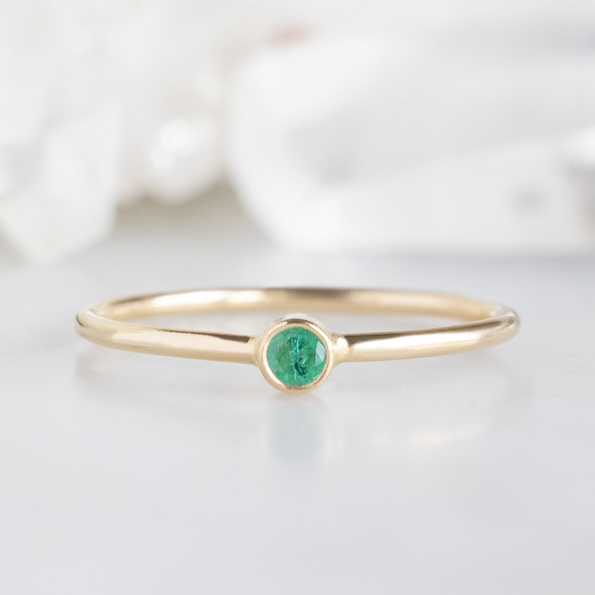 Custom Emerald Birthstone Stacking Ring | 10K Yellow Gold. Displayed on marble surface with white blurred background. 