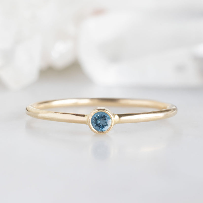 Custom Aquamarine Birthstone Stacking Ring | 10K Yellow Gold on marble surface with white blurred background.