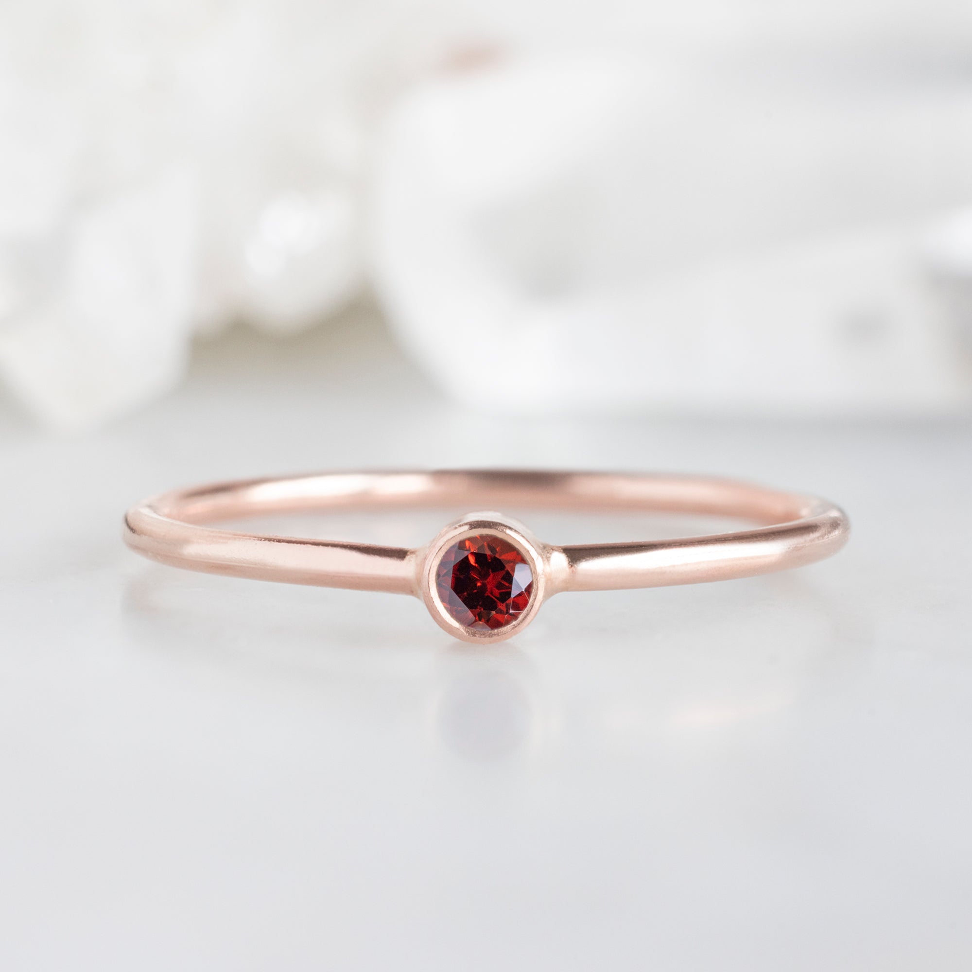 Custom Garnet Birthstone Stacking Ring | 10K Rose Gold. Displayed on marble surface with white blurred background. 