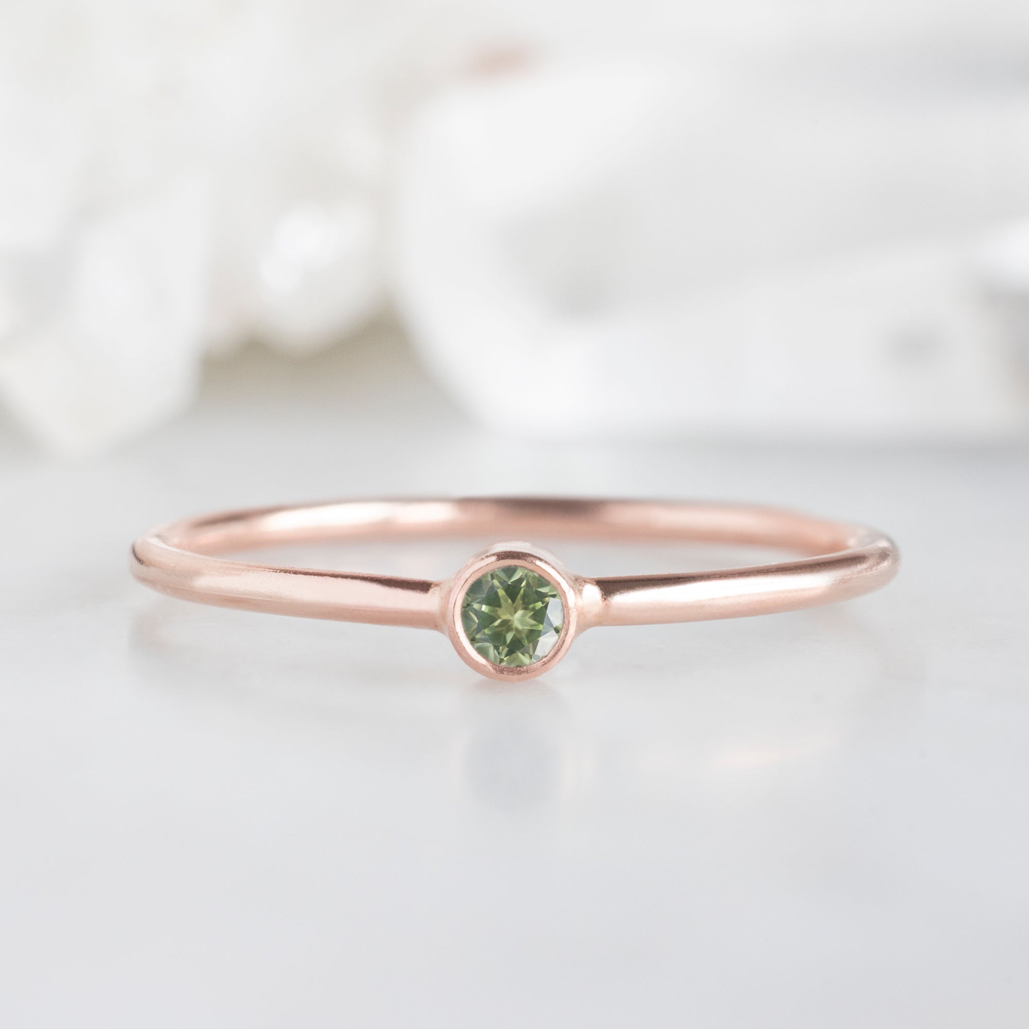 Custom Peridot Birthstone Stacking Ring | 10K Rose Gold. Displayed on marble surface with white blurred background. 